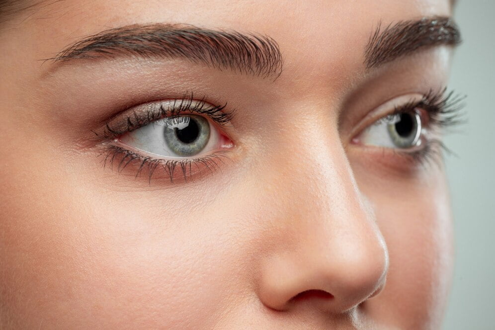 Close-up of a woman's eyes and nose, highlighting clear skin, well-groomed eyebrows, and healthy, hydrated eyes.