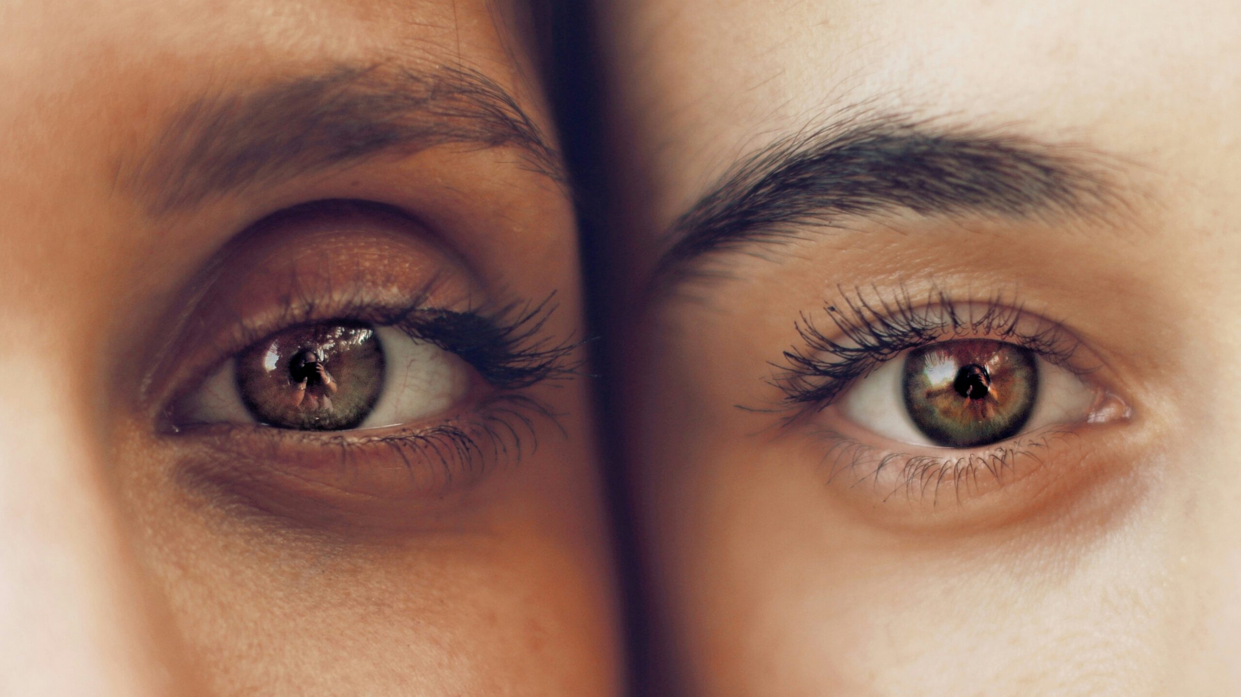 Close-up of two faces pressed side by side, focusing on their eyes with greenish-brown irises and long lashes.