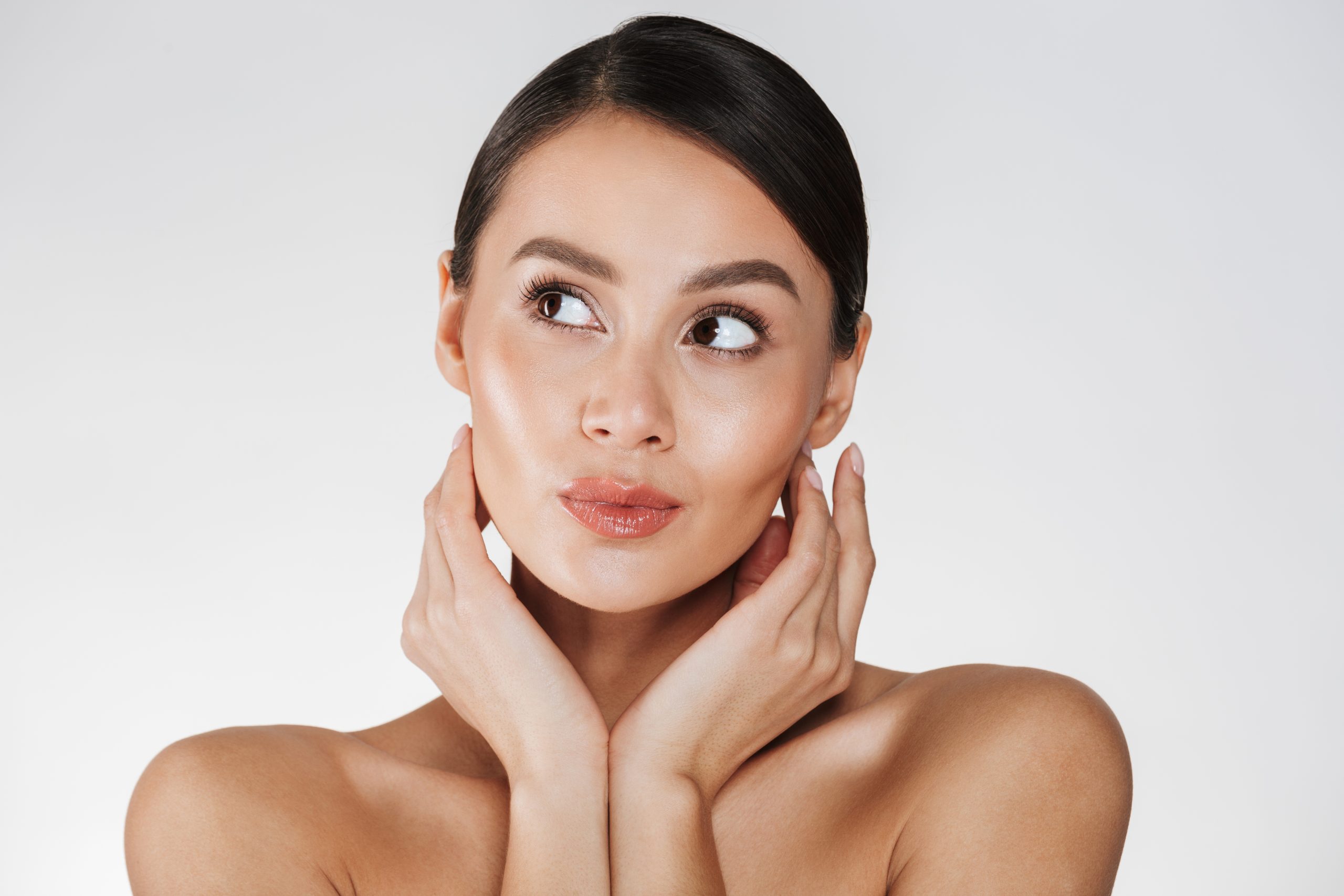 Close up portrait of beautiful woman with natural makeup looking aside and holding hands close to her healthy face isolated over white background