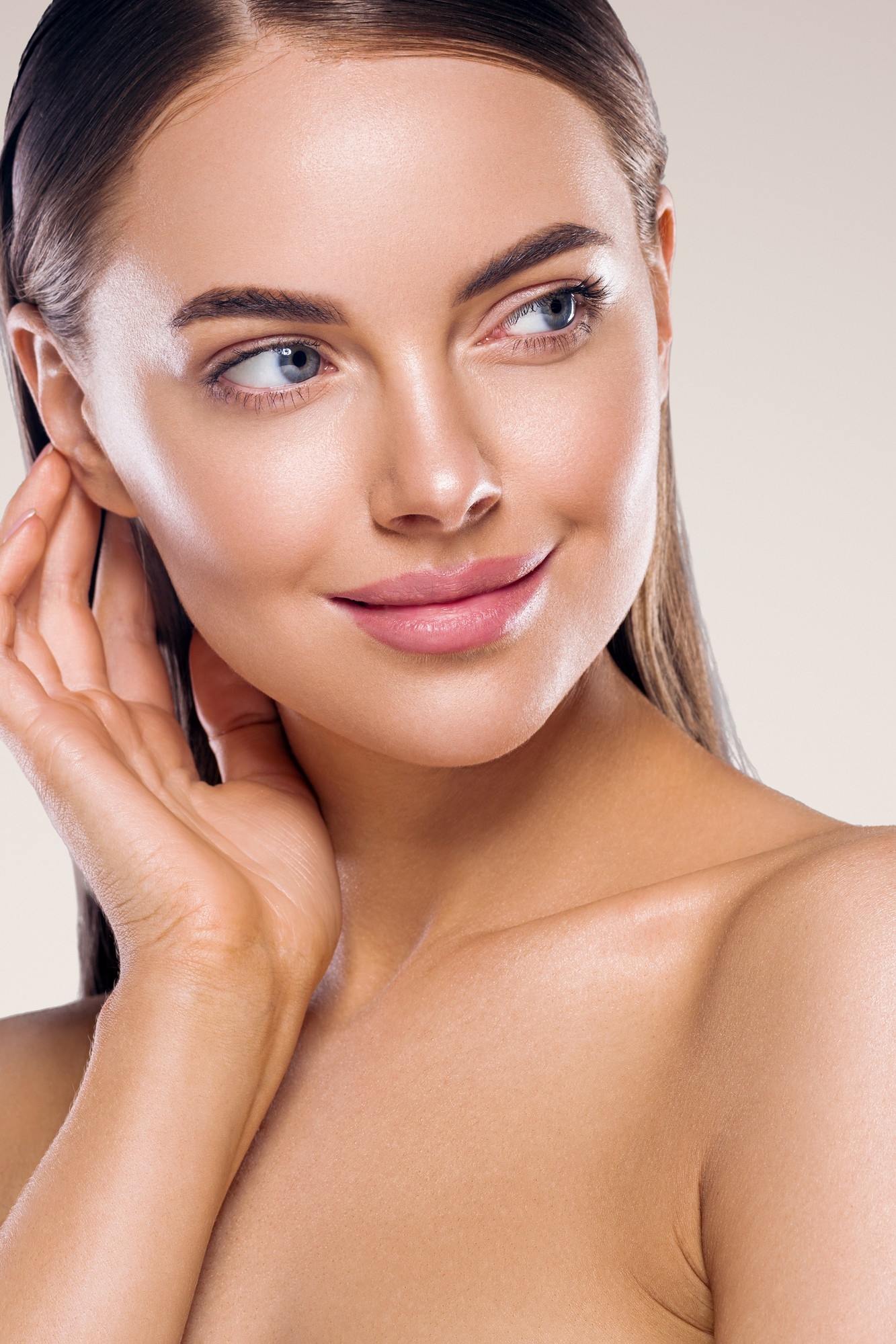 Close-up of a woman with glowing flawless skin, natural makeup, and smooth complexion touching her face gently.