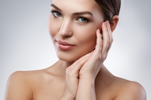 Portrait of a woman with radiant smooth skin, subtle makeup, and elegant pose with hands gently touching her face.