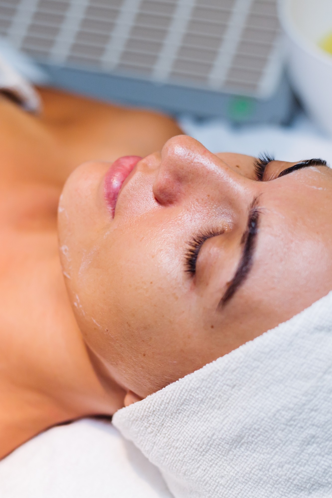Woman lying down with a towel wrap receiving a relaxing facial treatment.