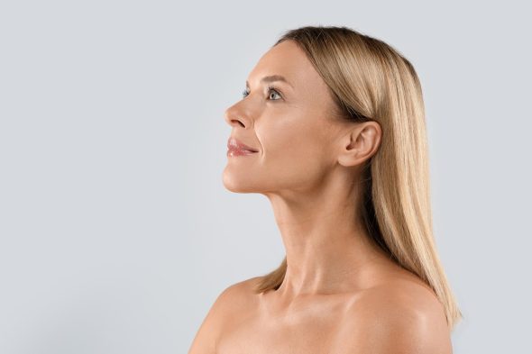 Profile of a woman with smooth, defined jawline and glowing skin looking upwards after aesthetic procedure.