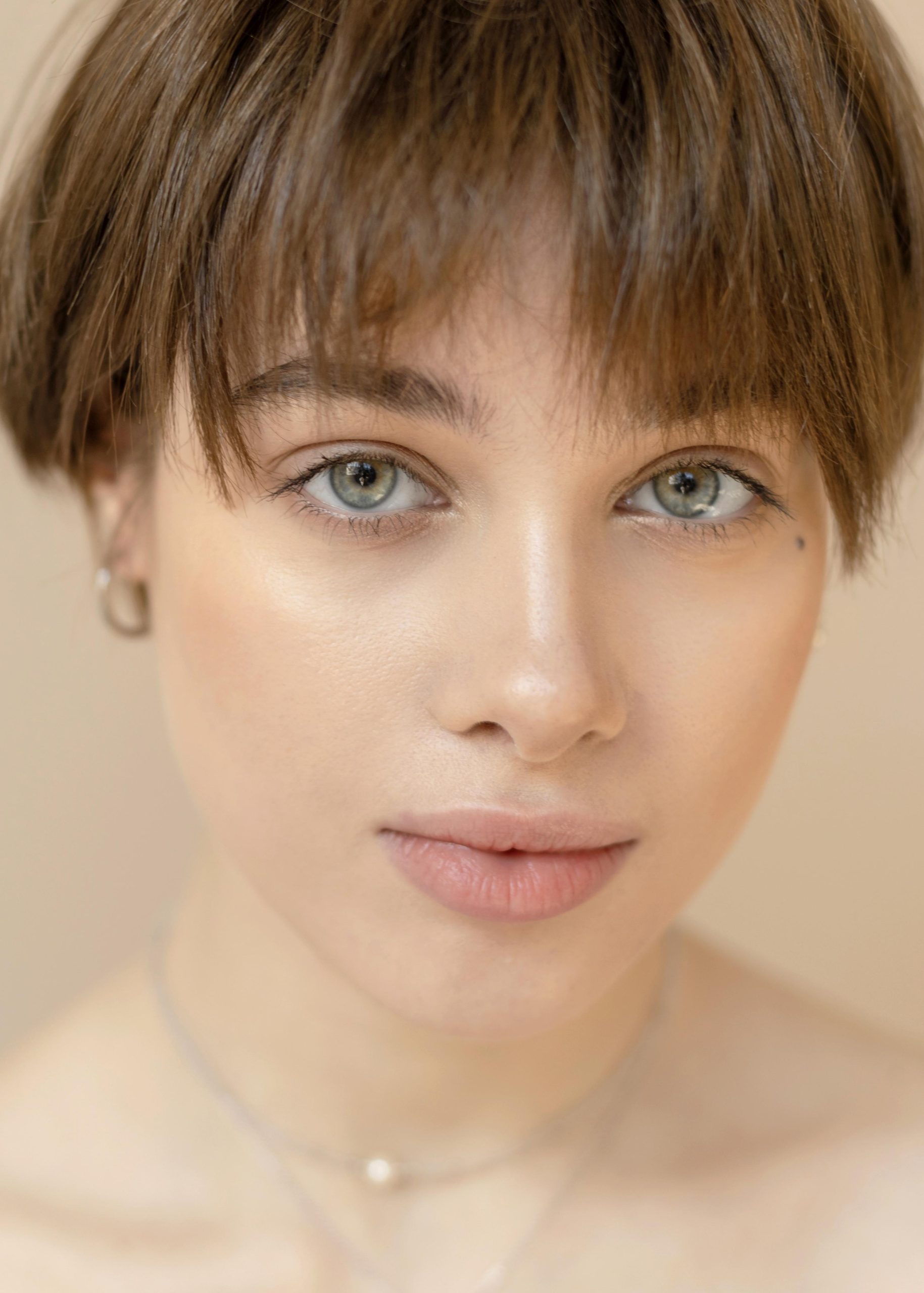 A soft-lit portrait of a young woman with short hair and radiant skin, showcasing a natural and confident expression.