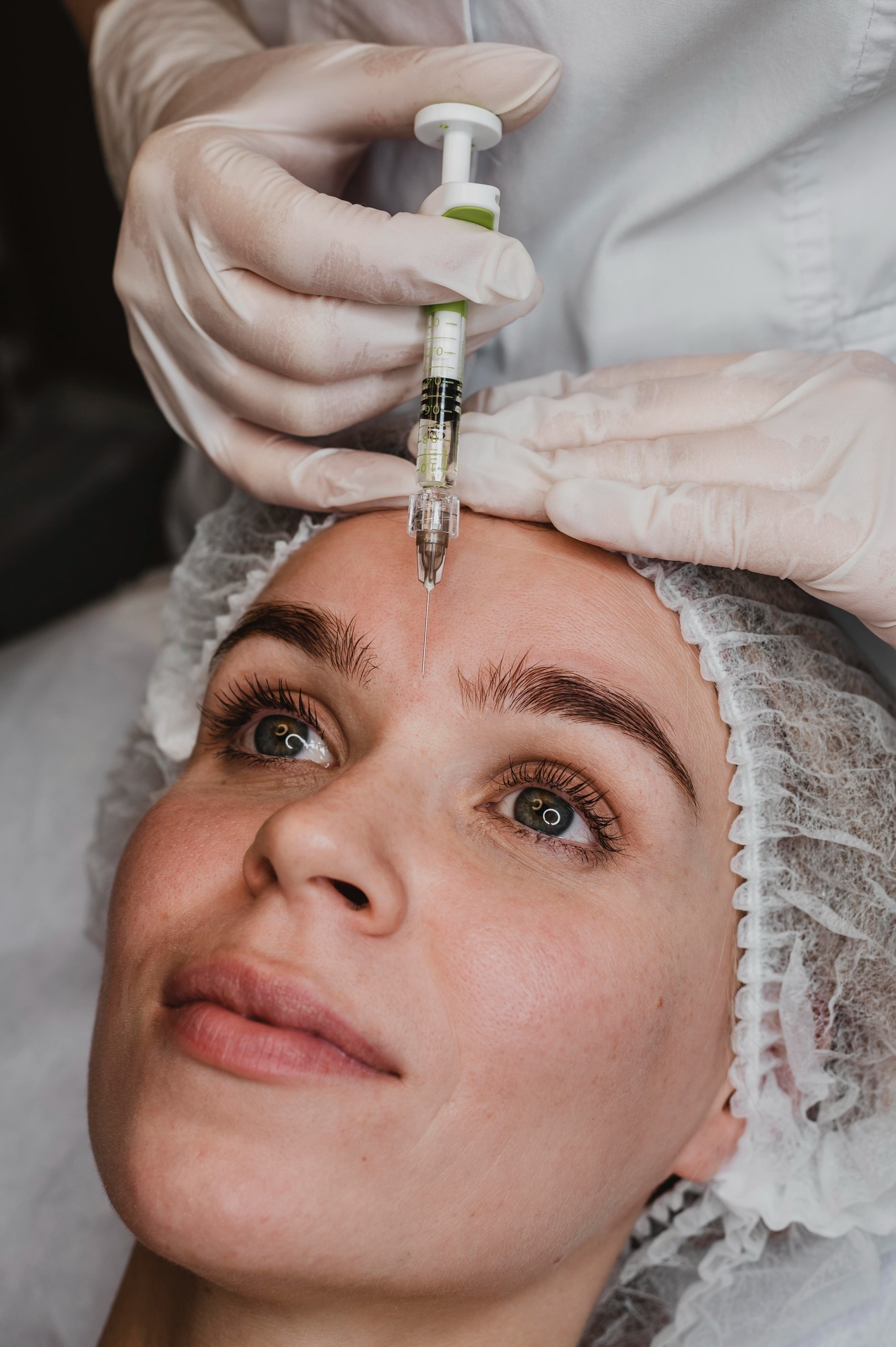 Close-up of a cosmetic facial injection being performed with a syringe on a woman lying in a clinical treatment setting.