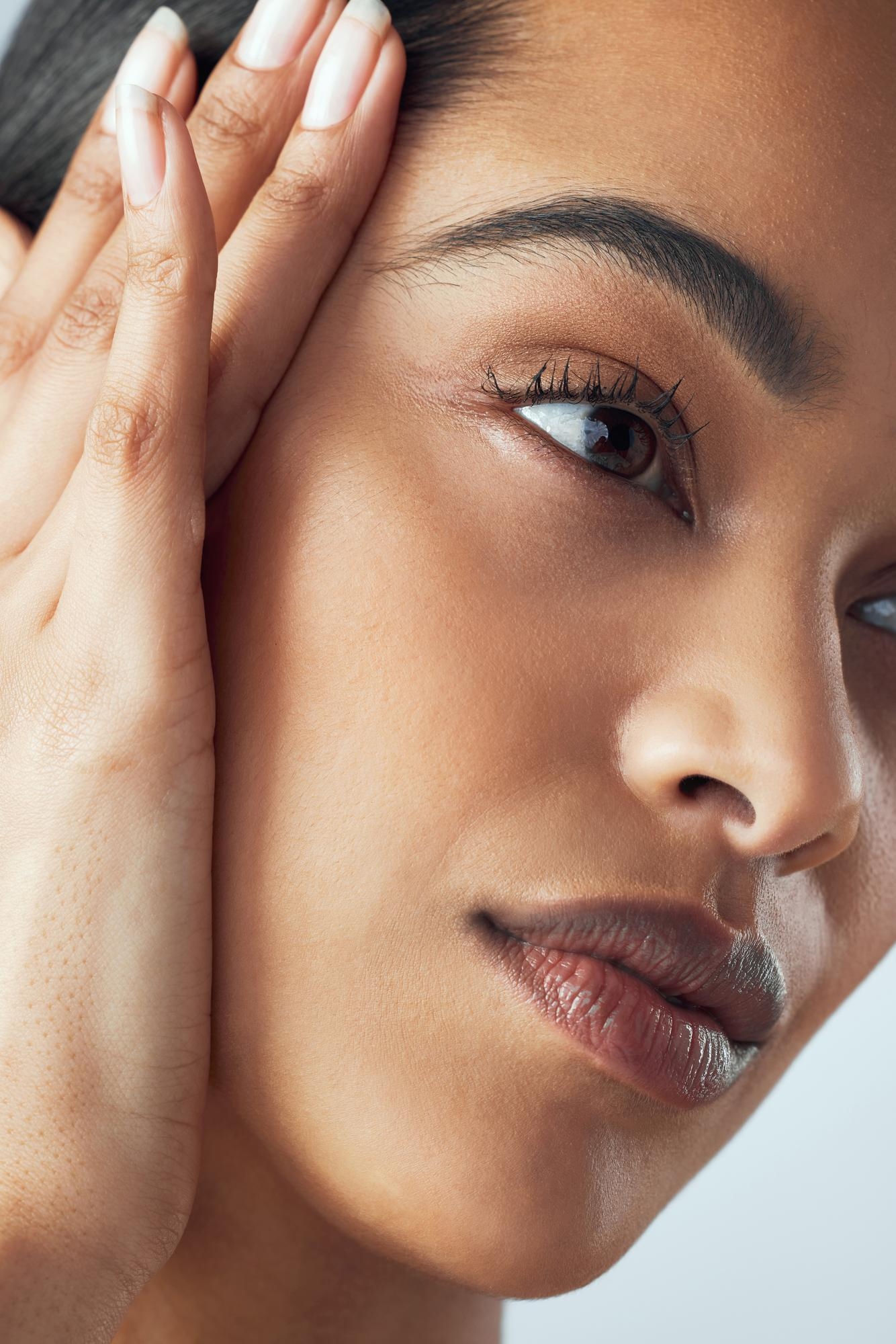 Close-up of a woman resting her hand against her temple, showing natural makeup and smooth skin.