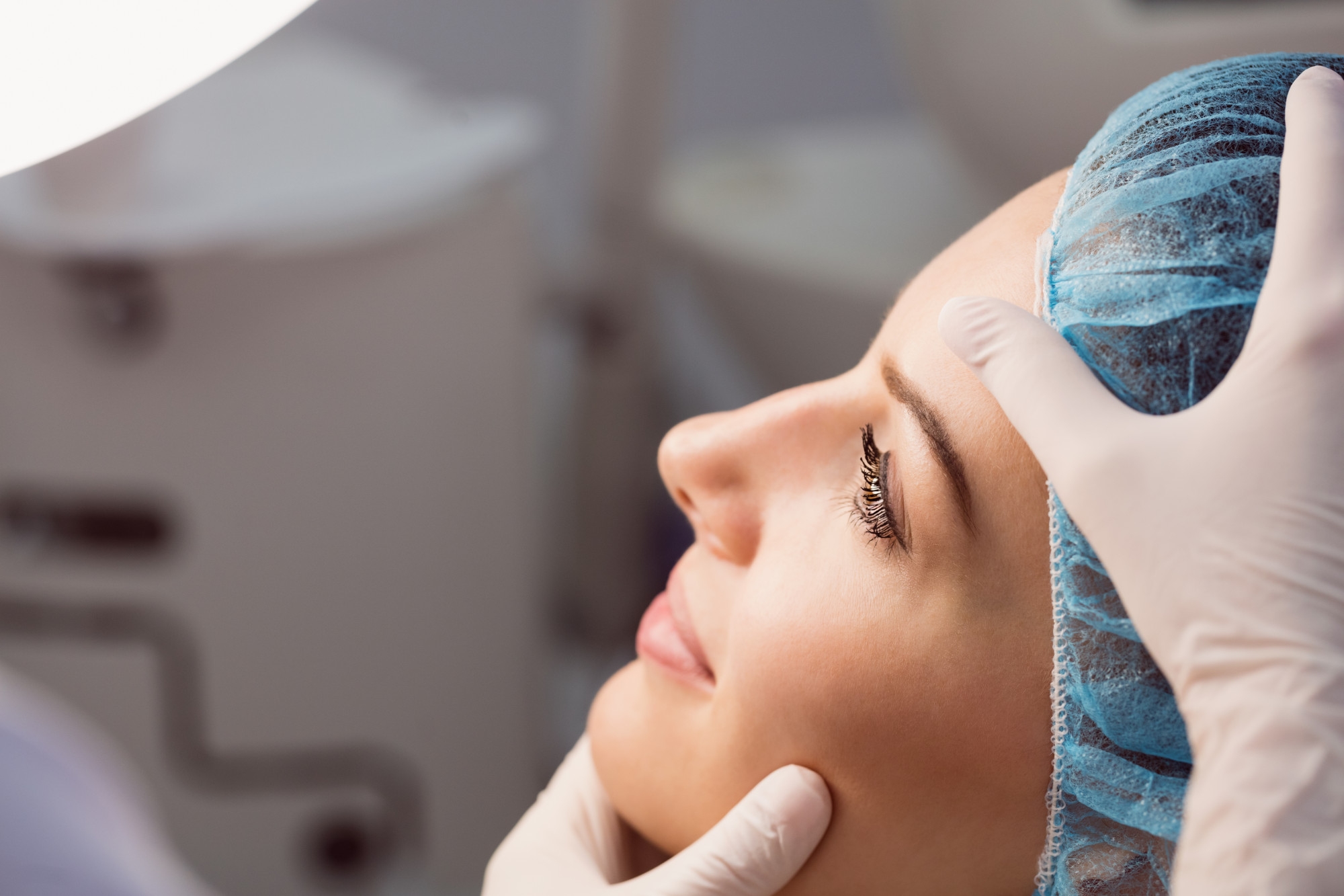 Woman lying down during a facial examination while wearing a medical cap in a clinical setting.