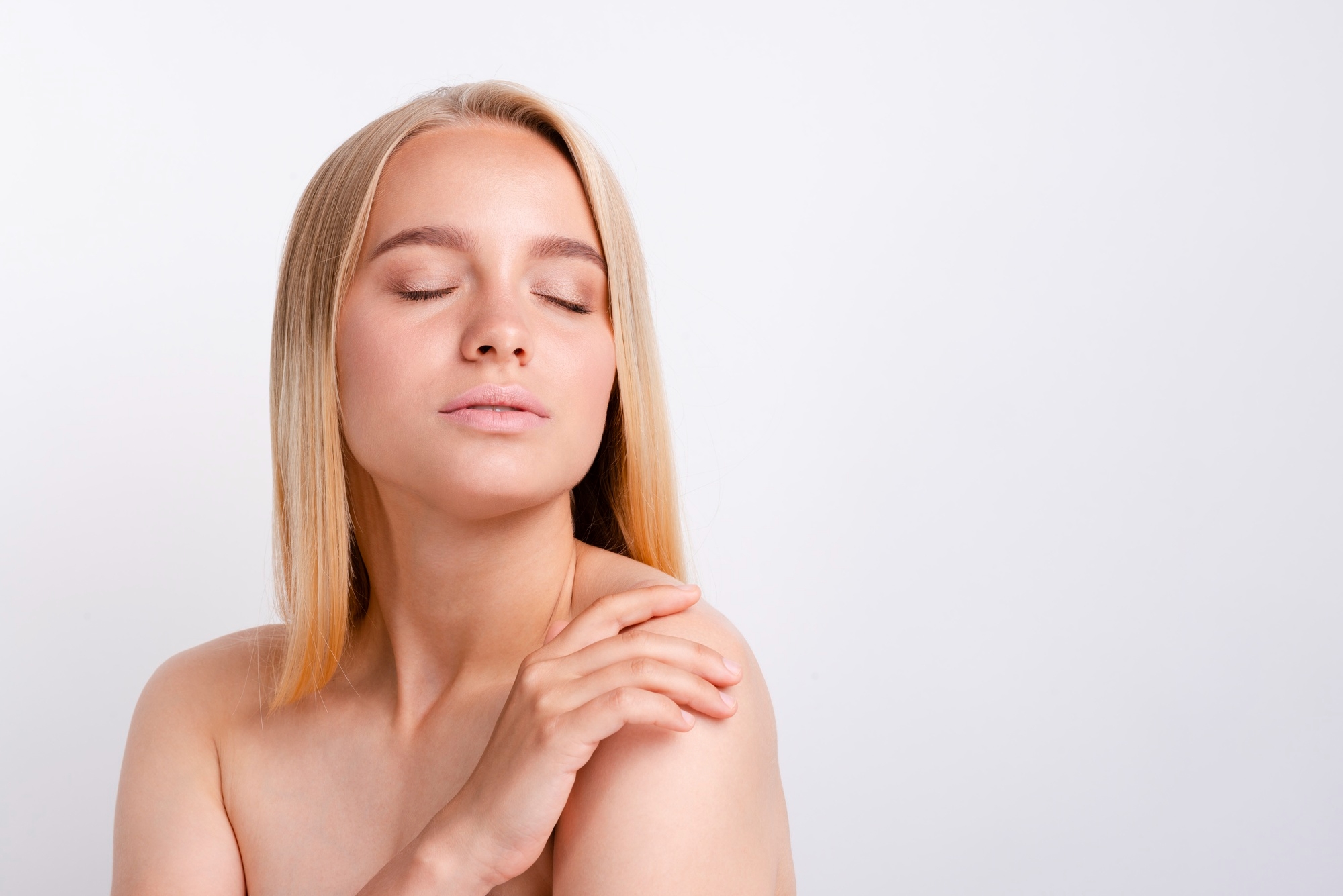 Woman with eyes closed resting her hand on her shoulder, conveying calmness and skin wellness.