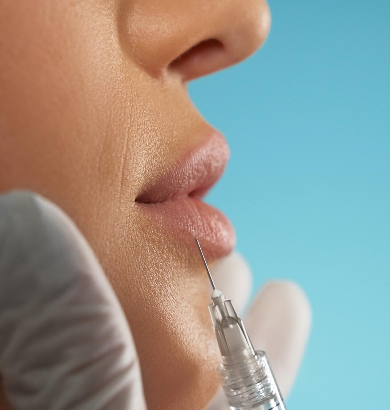 Woman with eyes closed receiving a lip filler injection from a practitioner wearing blue medical gloves.