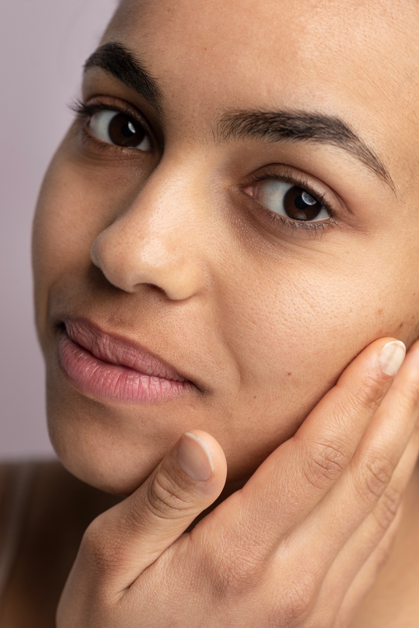 Close-up of a woman touching her cheek, showcasing natural skin texture and a calm expression.