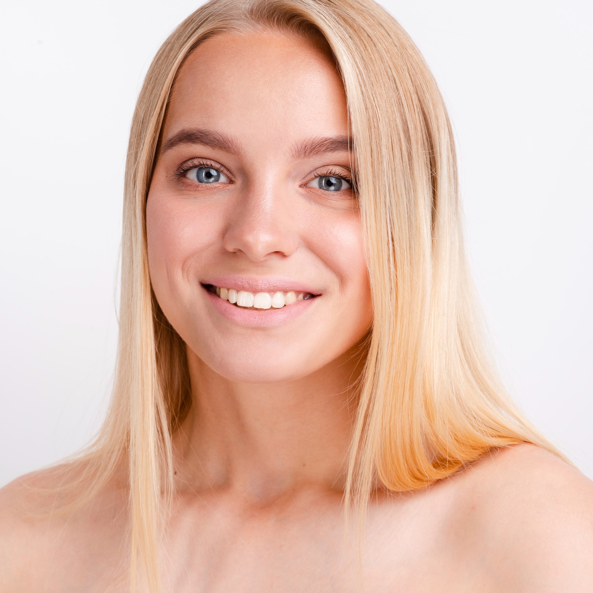 Portrait of a smiling blonde woman with minimal makeup and clear skin against a white background.