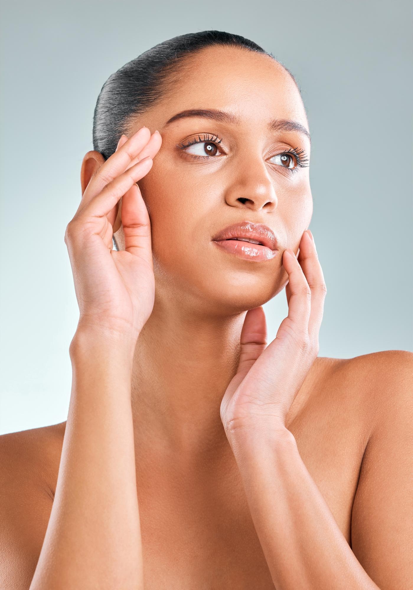 Woman gently touching her face with both hands, showcasing smooth skin and a thoughtful expression.