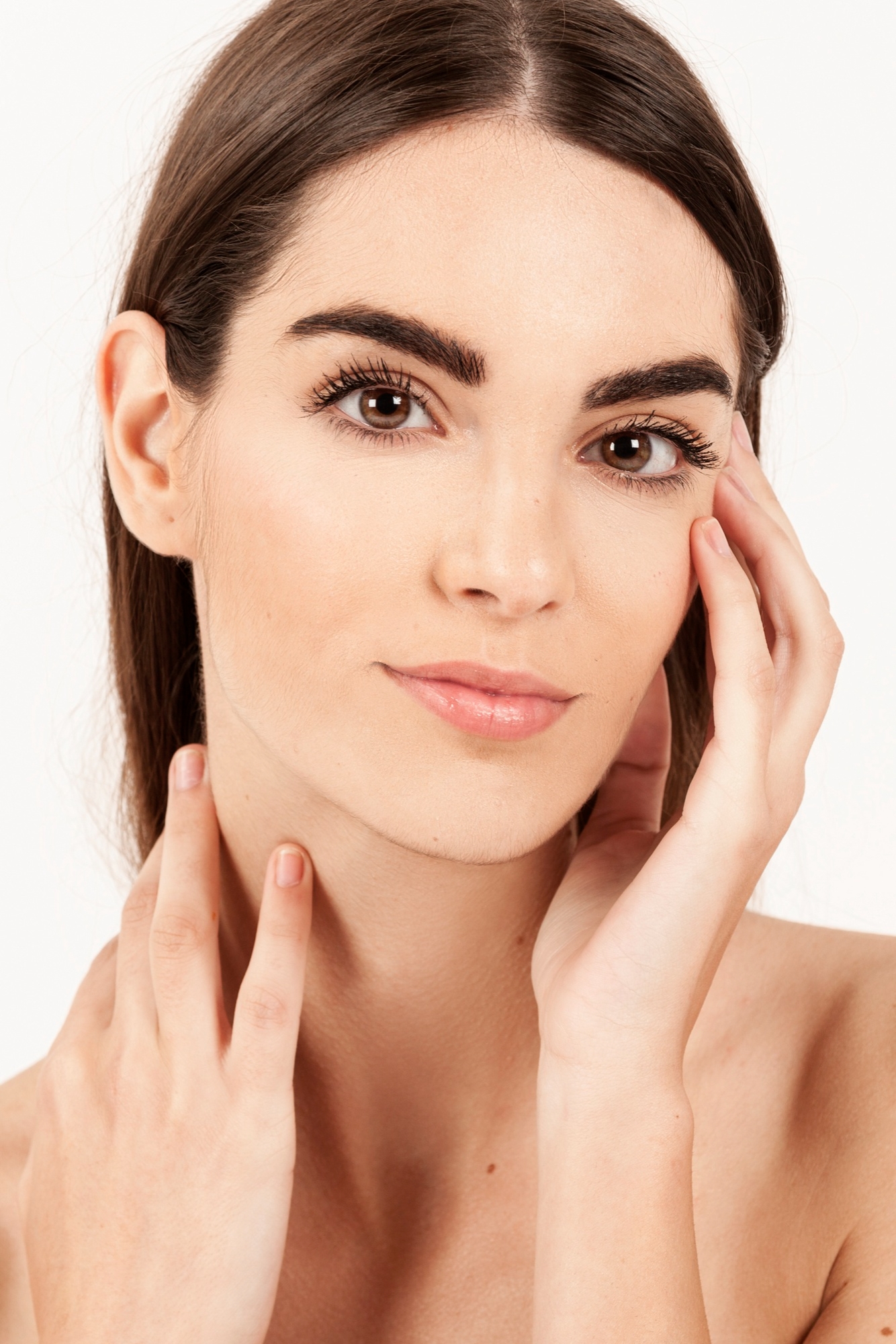 Portrait of a young woman with smooth skin and natural makeup touching her face against a white background.