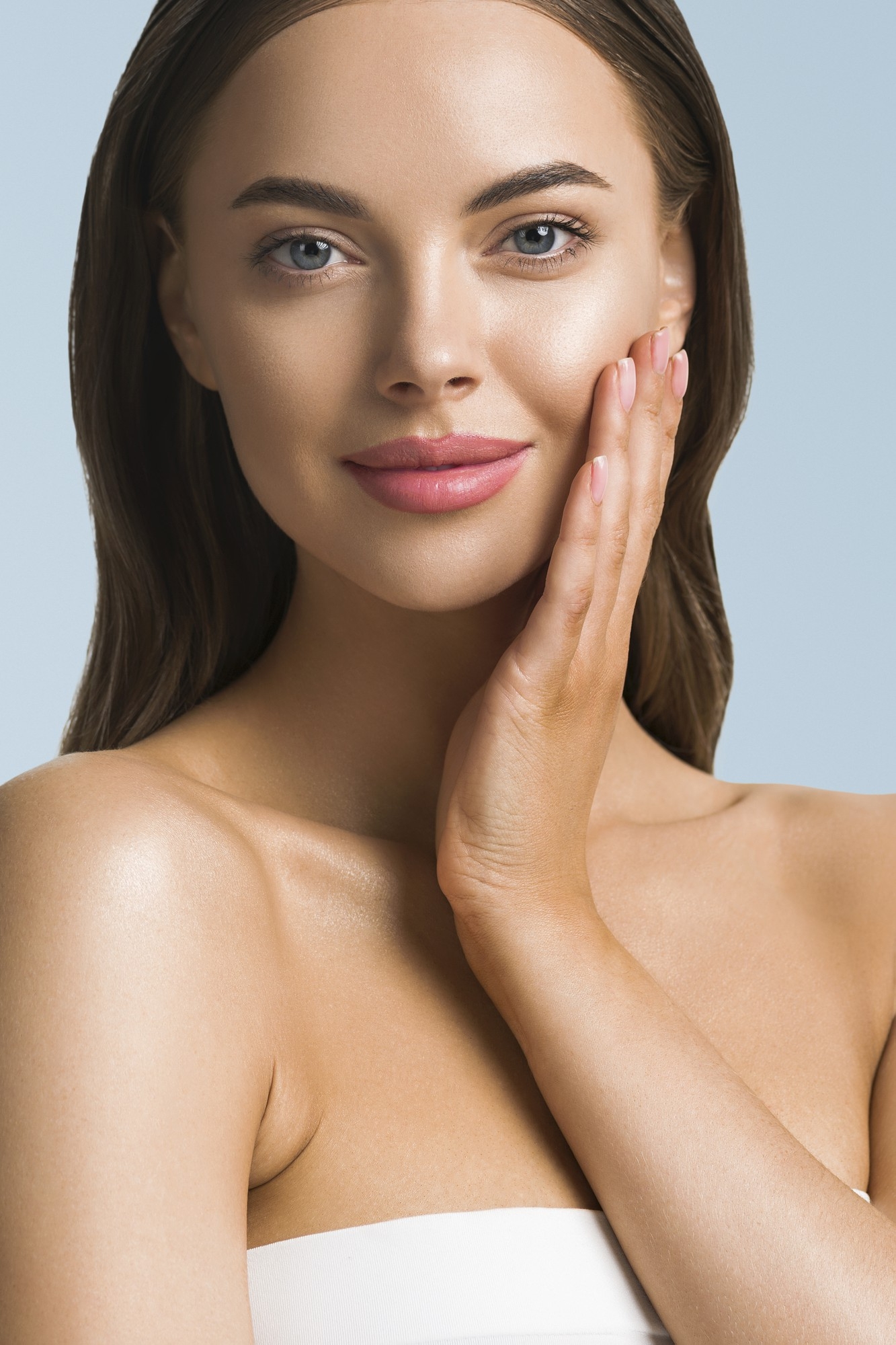 Beauty portrait of a woman with smooth skin gently touching her cheek against a neutral background.