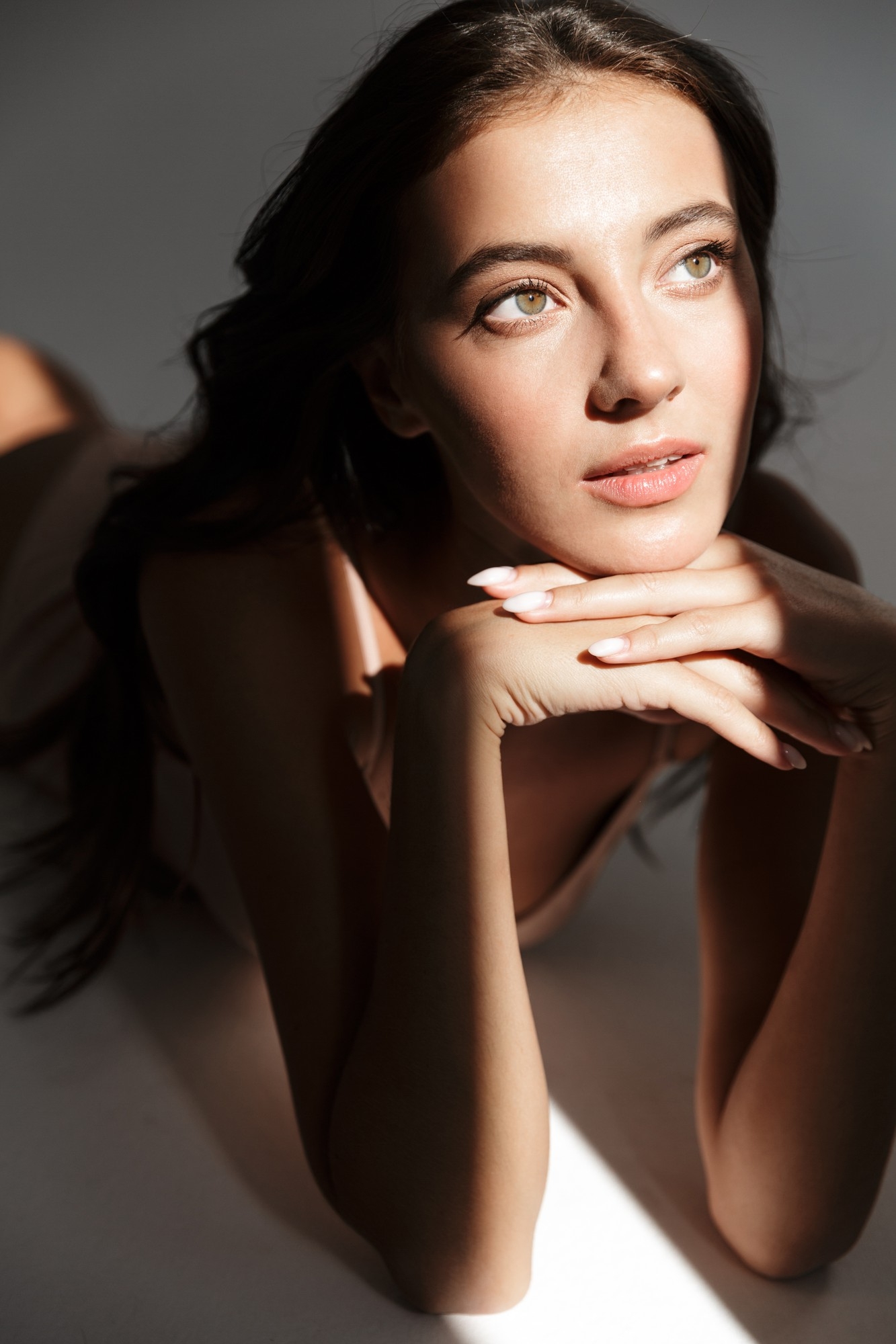 Close-up of a woman with glowing skin resting her chin on her hands, illuminated by dramatic side lighting.