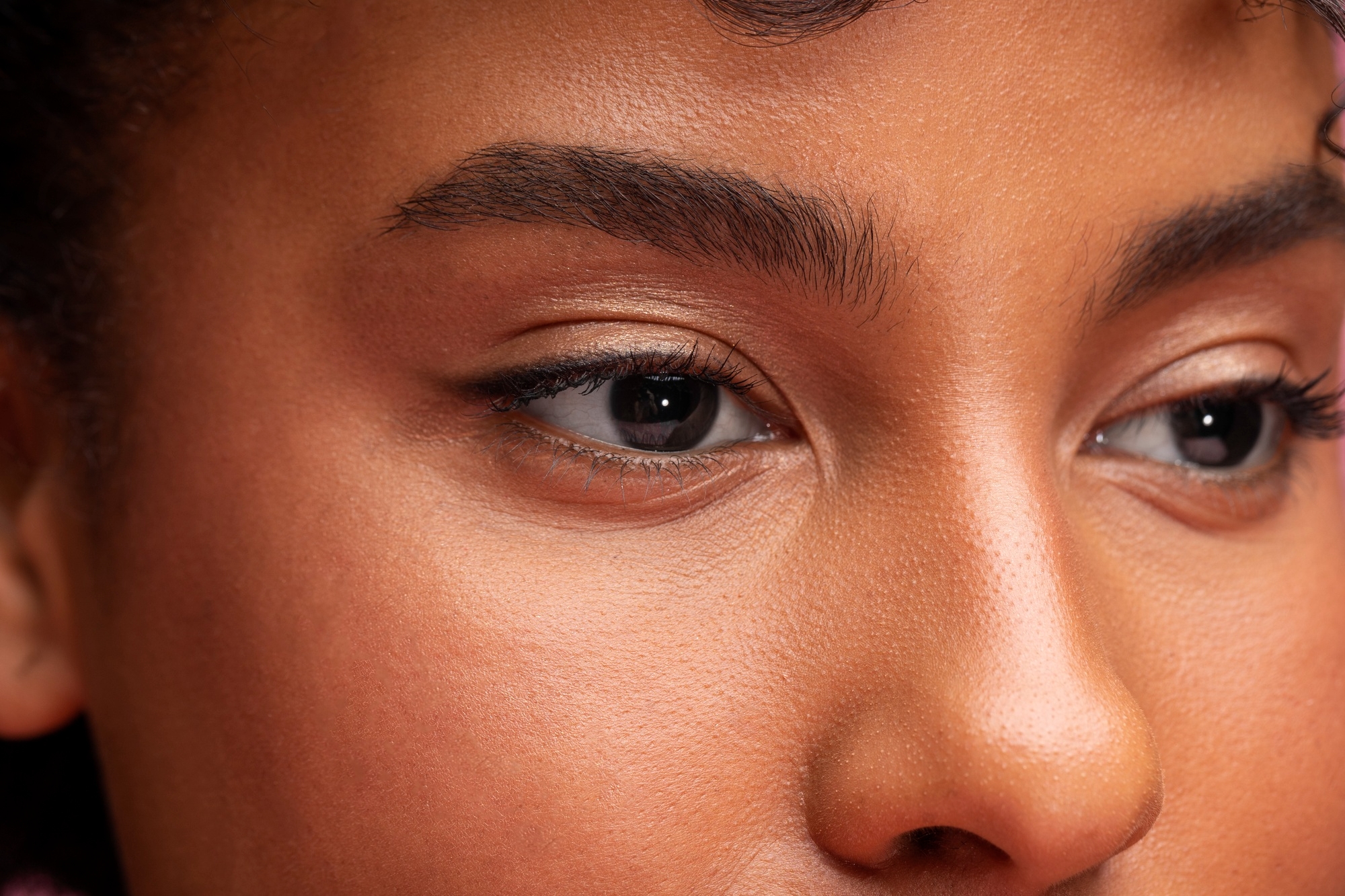 Extreme close-up of a face highlighting eyes, eyebrows, and smooth skin texture with warm lighting and neutral makeup.