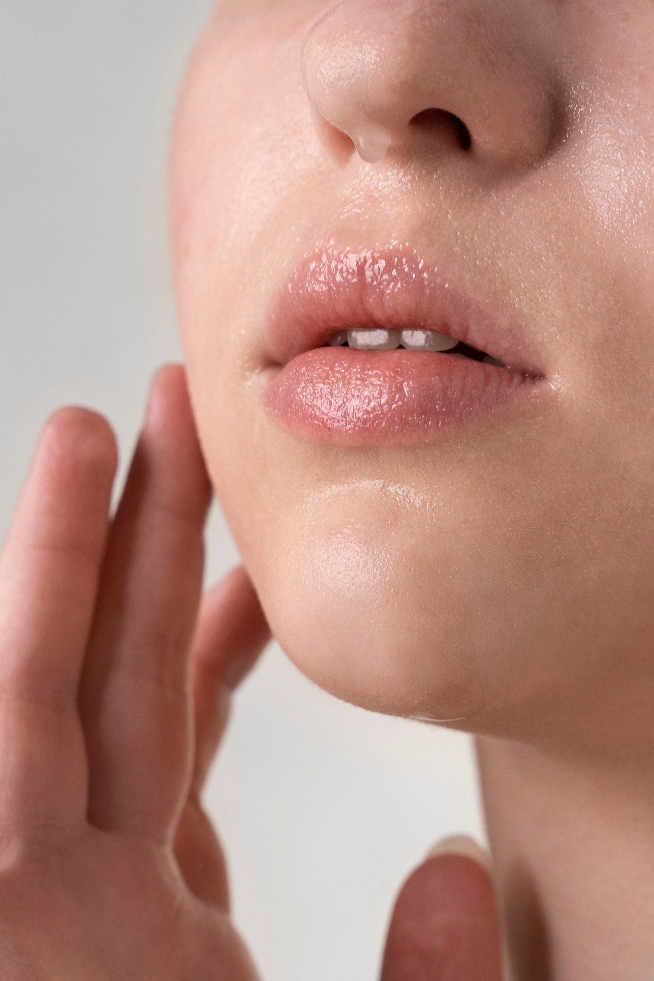 Close-up of glossy lips and chin with a hand touching the face, showing radiant moisturized skin.