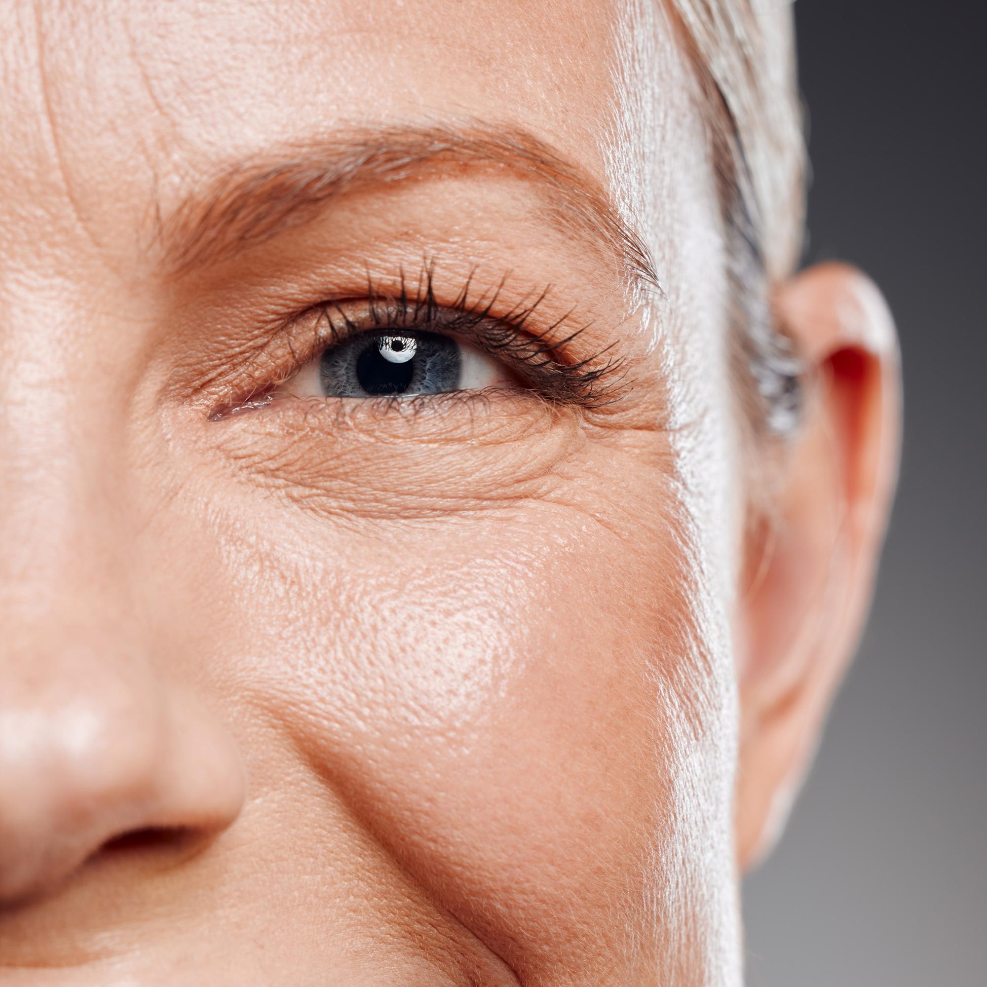 Detailed close-up of an older woman’s eye showing crow’s feet and natural skin texture in soft lighting.