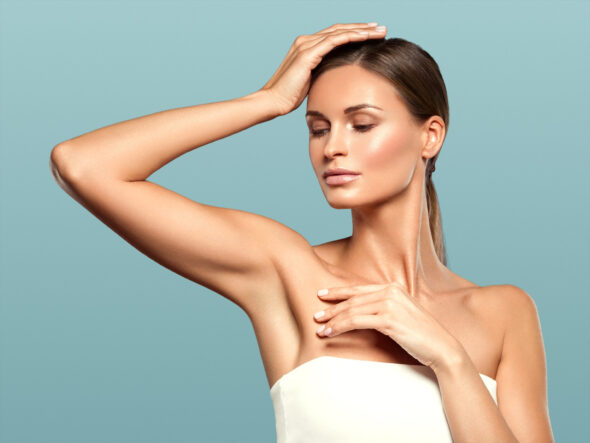 Woman with smooth underarm skin posing with one arm raised against a soft blue background.