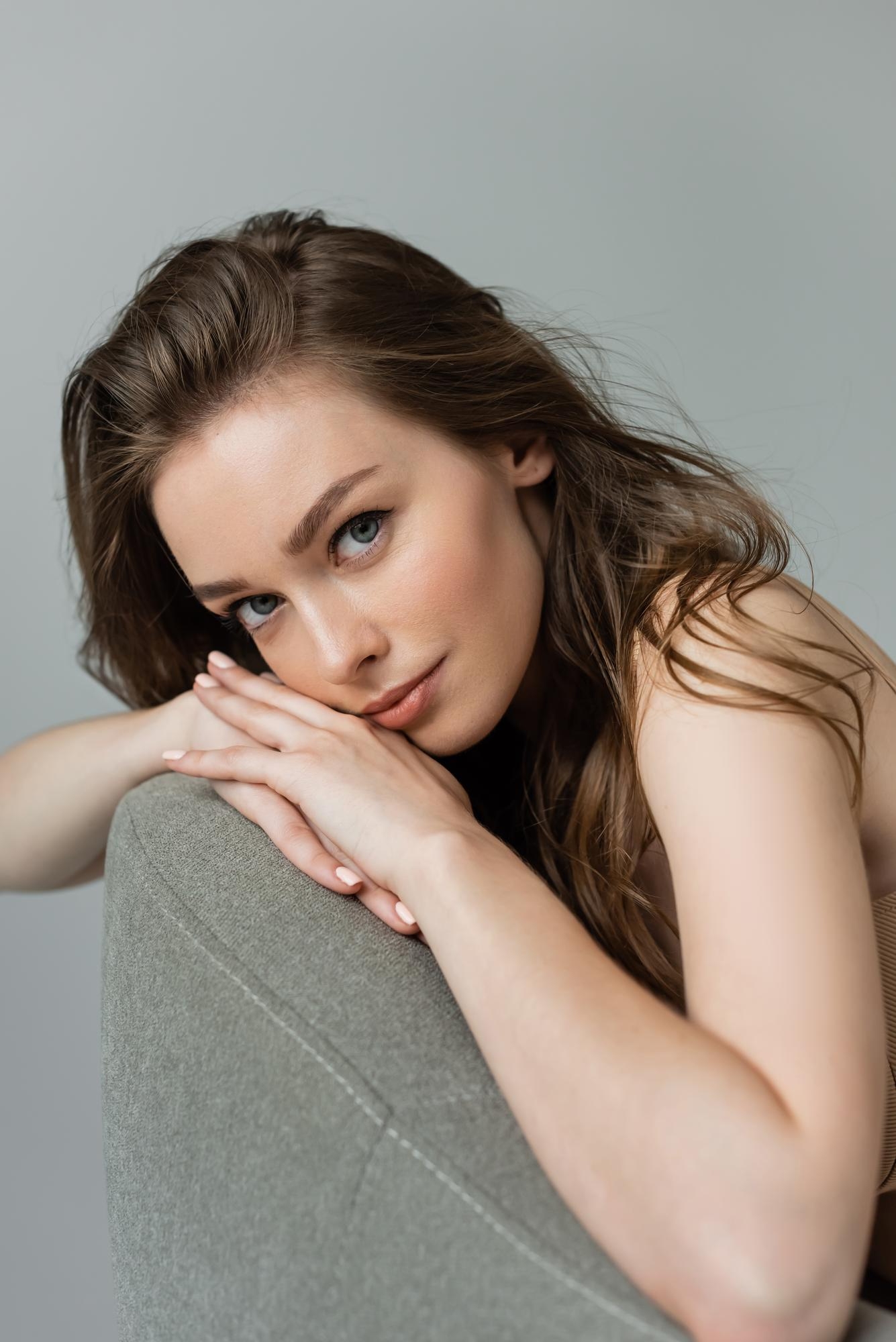 Woman with long light brown hair resting her head on her folded arms over a chair, gazing at the camera.