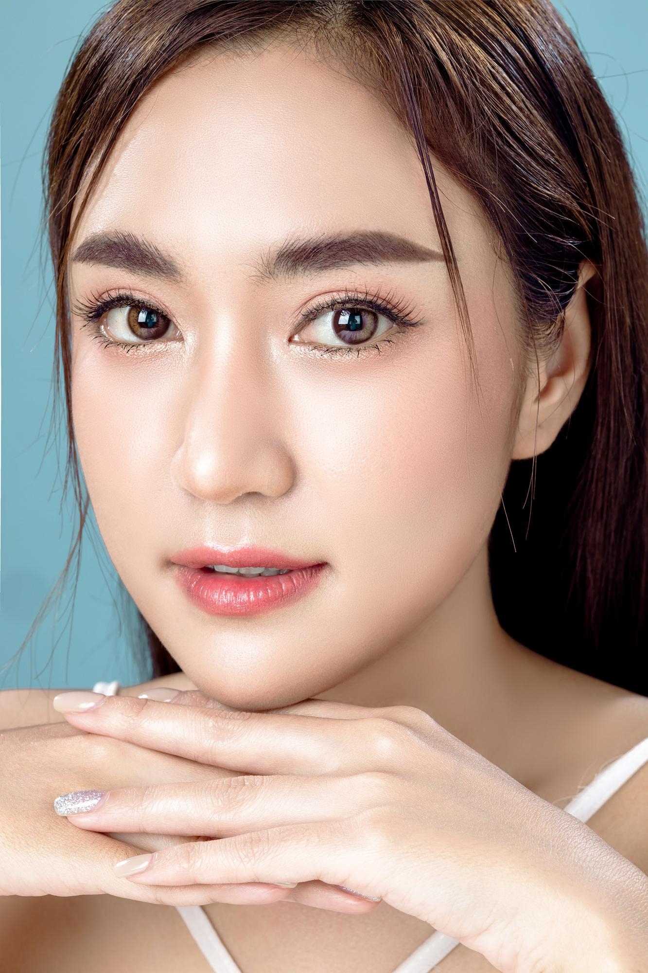 Beauty portrait of a woman resting her hands under her chin against a light blue background.