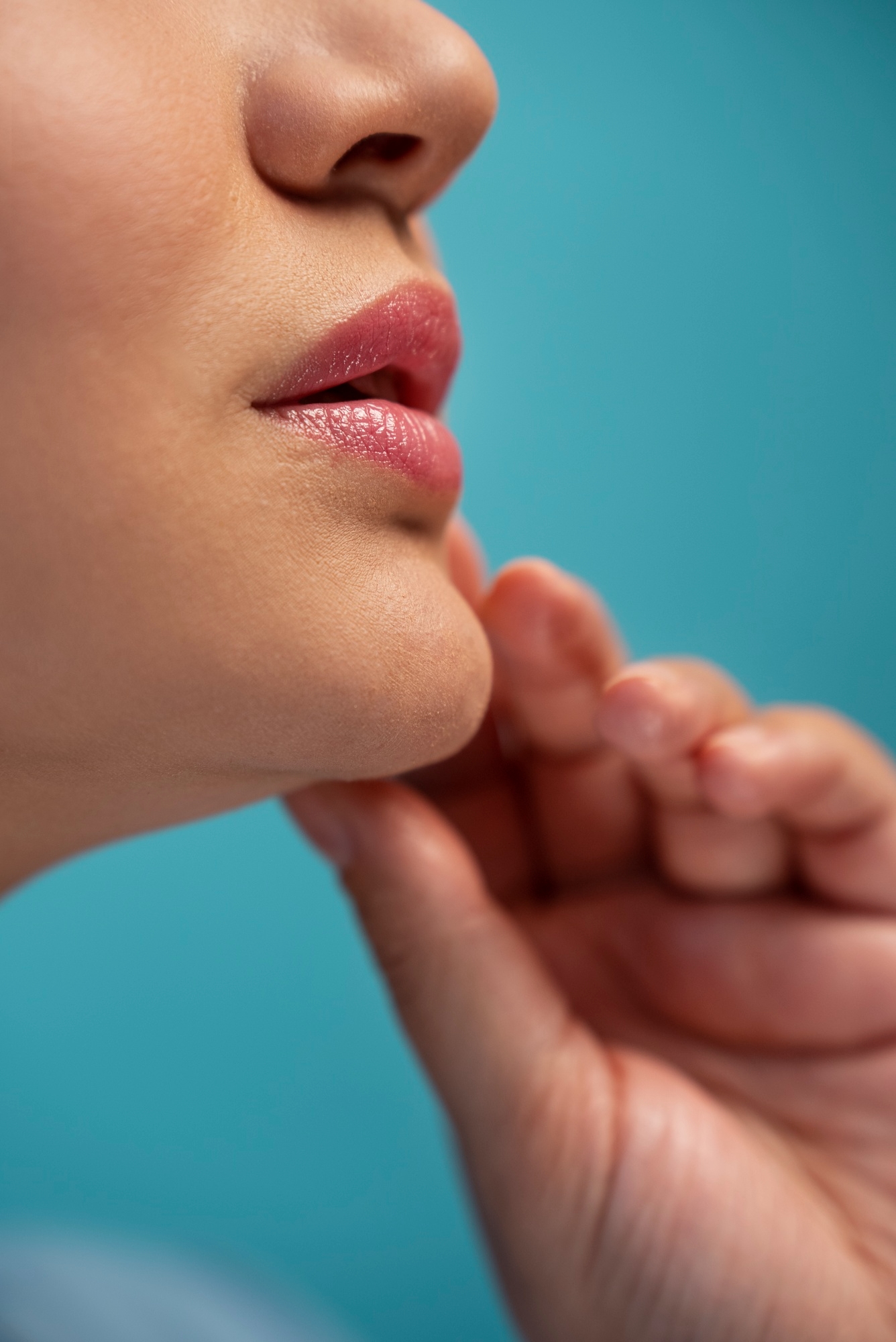 Close-up of lips and chin with fingers resting below the jaw against a blue background.