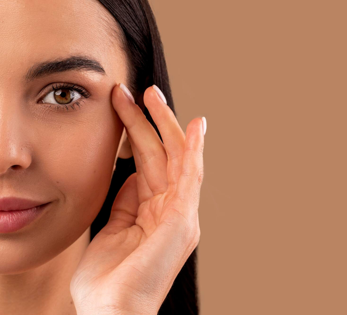 Close-up of half a woman’s face touching the skin near her eye against a beige background
