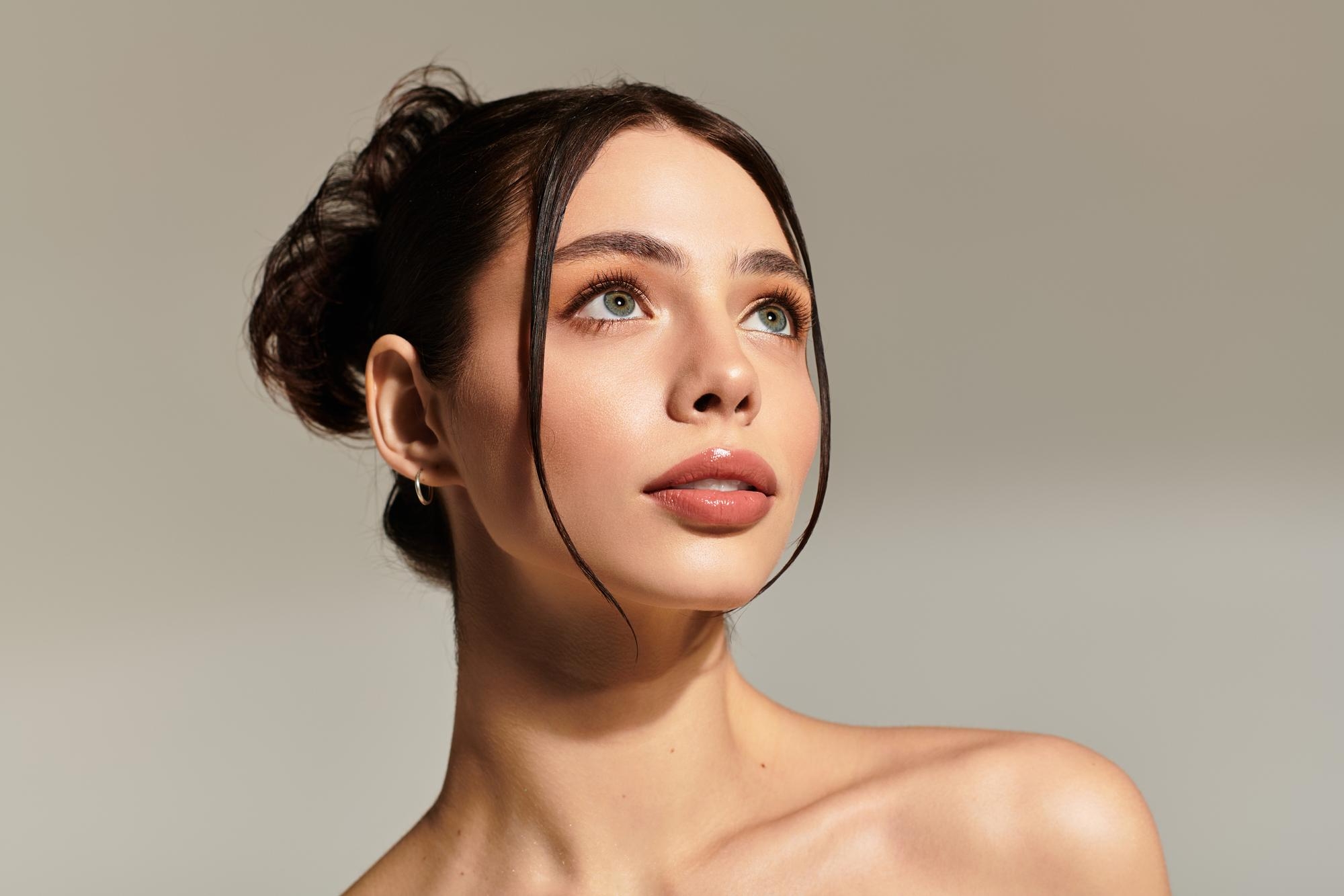 Studio portrait of a woman with dark hair in an updo looking upward with soft lighting and a neutral background.