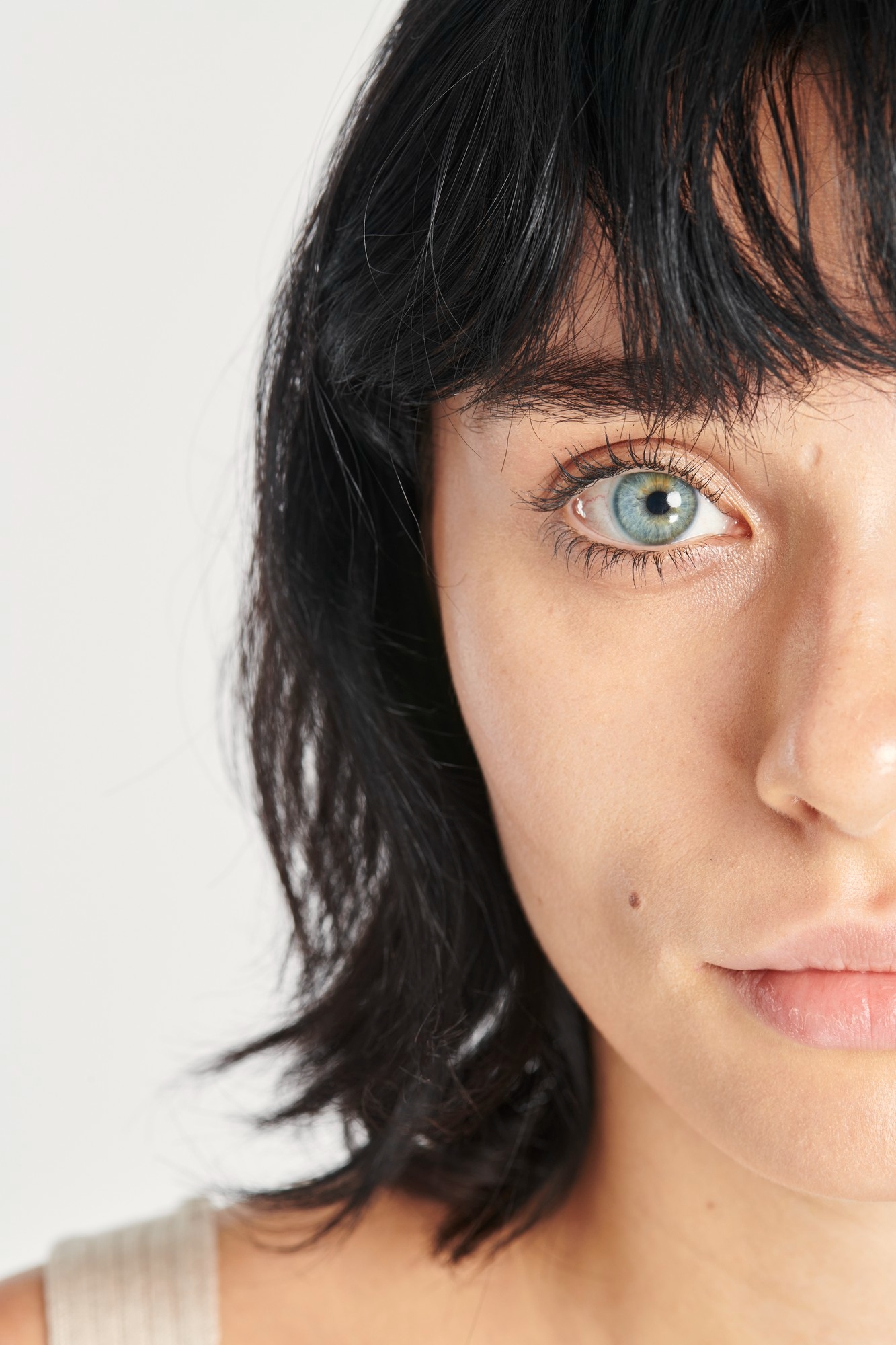 Half-face portrait of a woman with a dark bob haircut and blue eye looking at the camera against a light background.