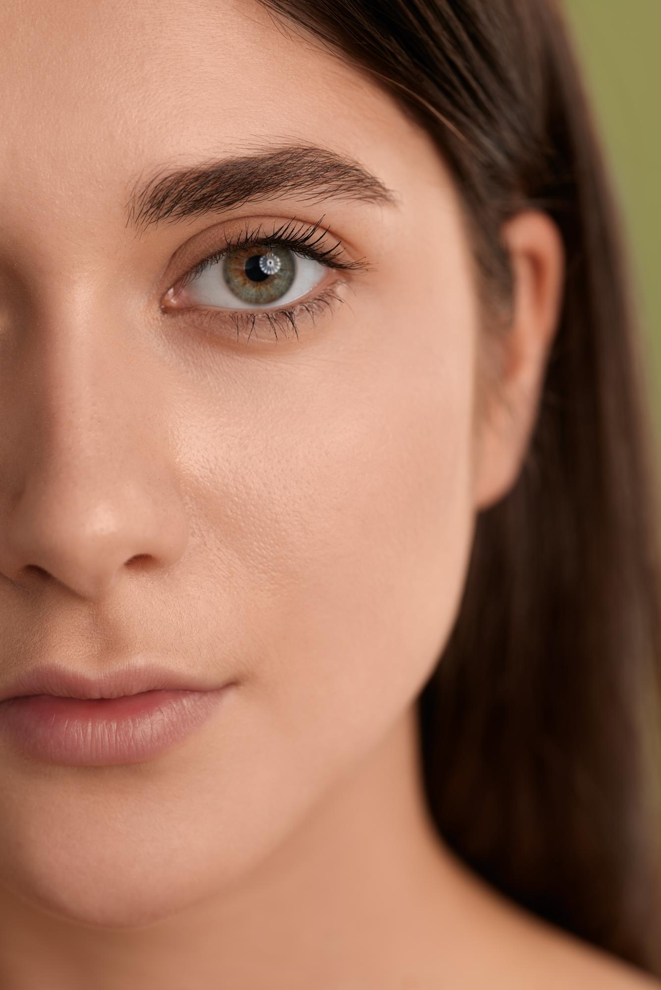 Half-face portrait of a woman with a green eye and natural skin texture against a soft background.