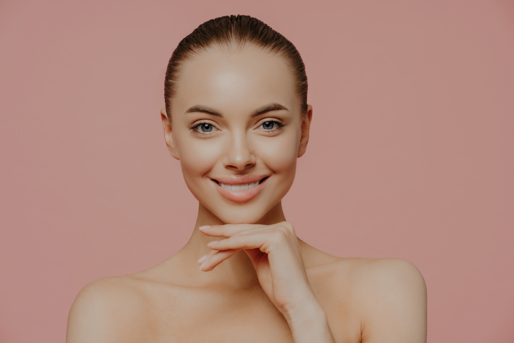 Smiling woman with clear skin posing against a pink background.
