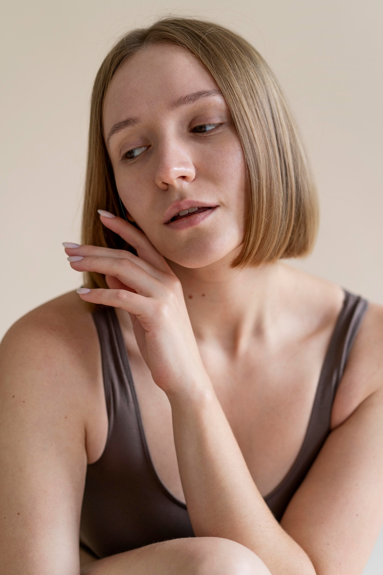 Portrait of a woman in a sleeveless top gently touching her face in soft natural light.