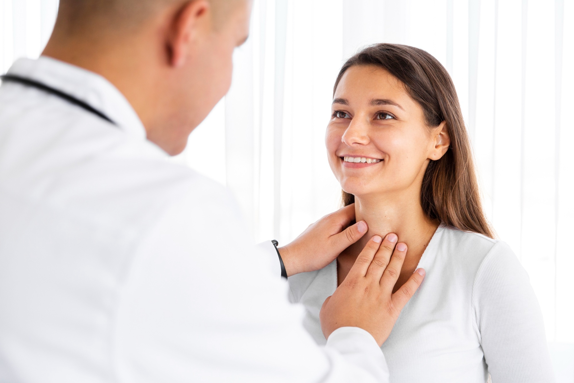Doctor examining a smiling patient’s neck during a thyroid or throat checkup.