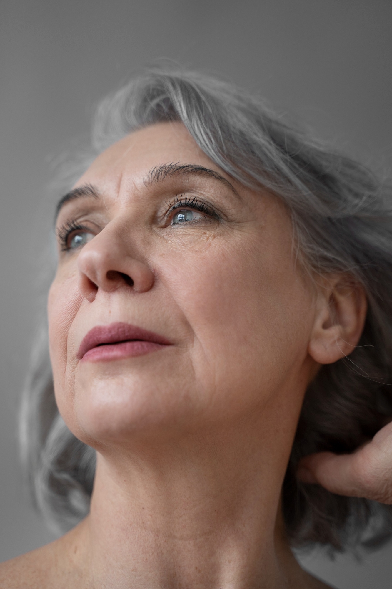 Mature beauty portrait of a woman with gray hair looking upward, highlighting natural skin texture and soft facial lines.