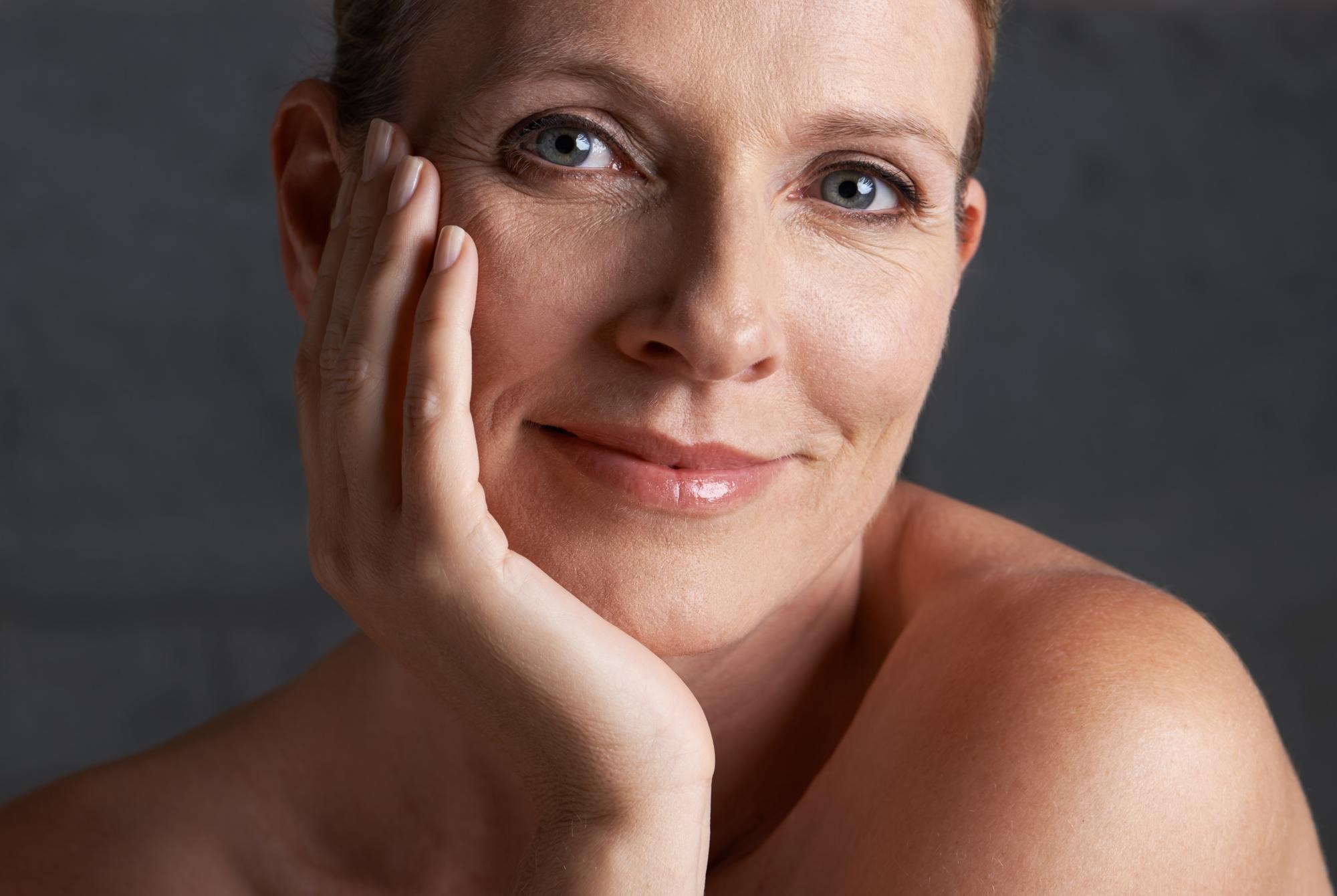 Mature beauty portrait of a smiling woman resting her face on her hand, showing natural skin texture and a soft expression.