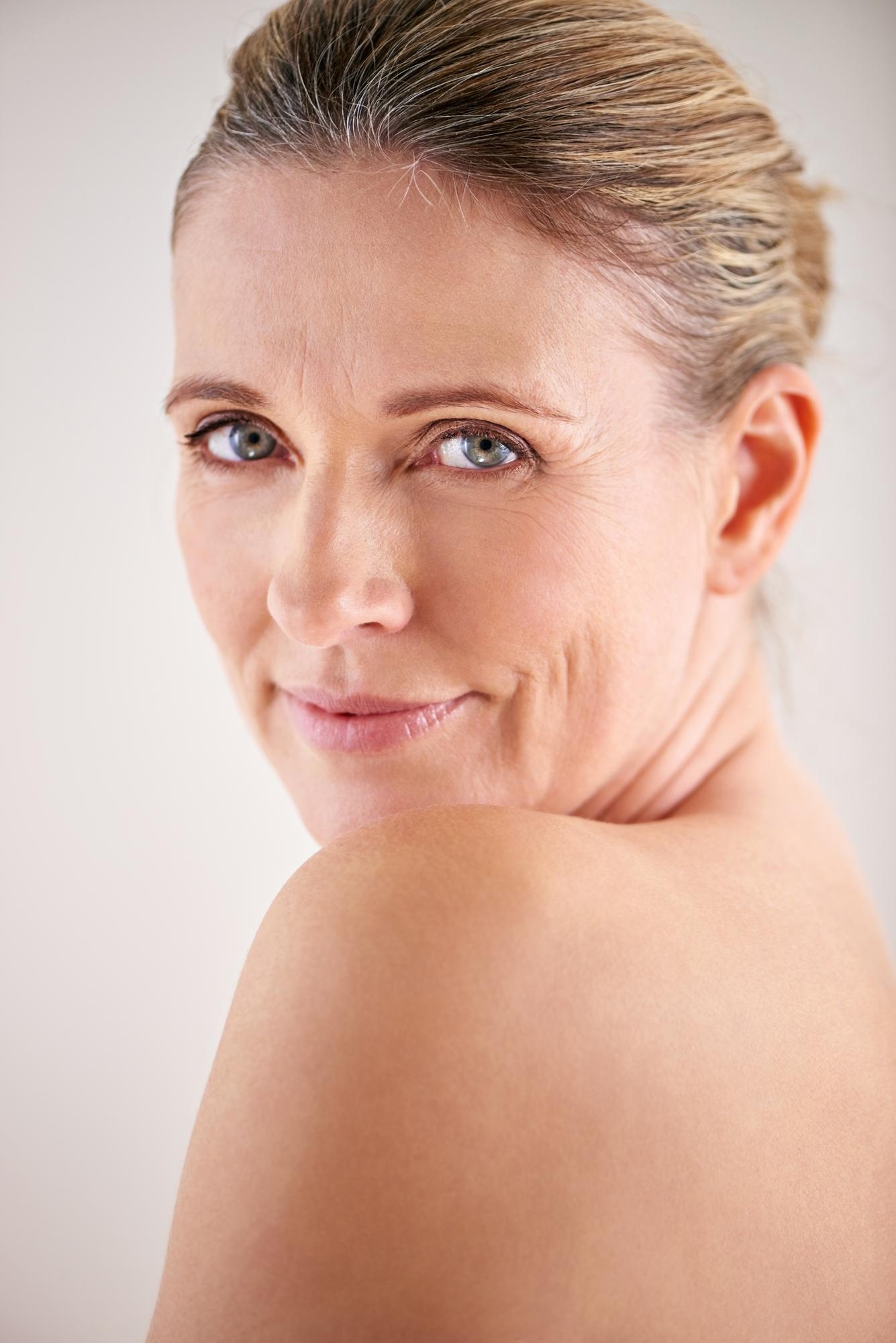Mature beauty portrait of a smiling woman looking over her shoulder with smooth skin and subtle facial lines.
