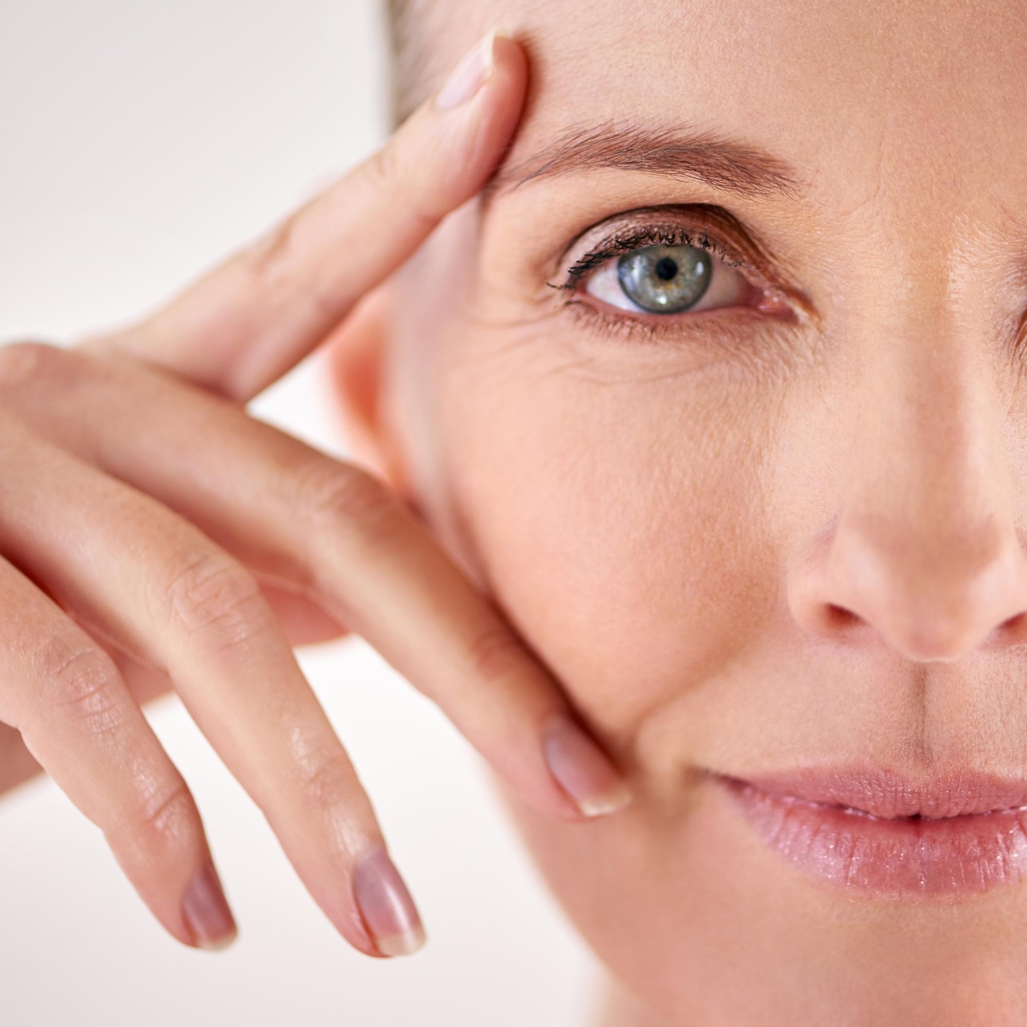 Close-up of a mature woman touching the skin near her eye, showing natural fine lines.