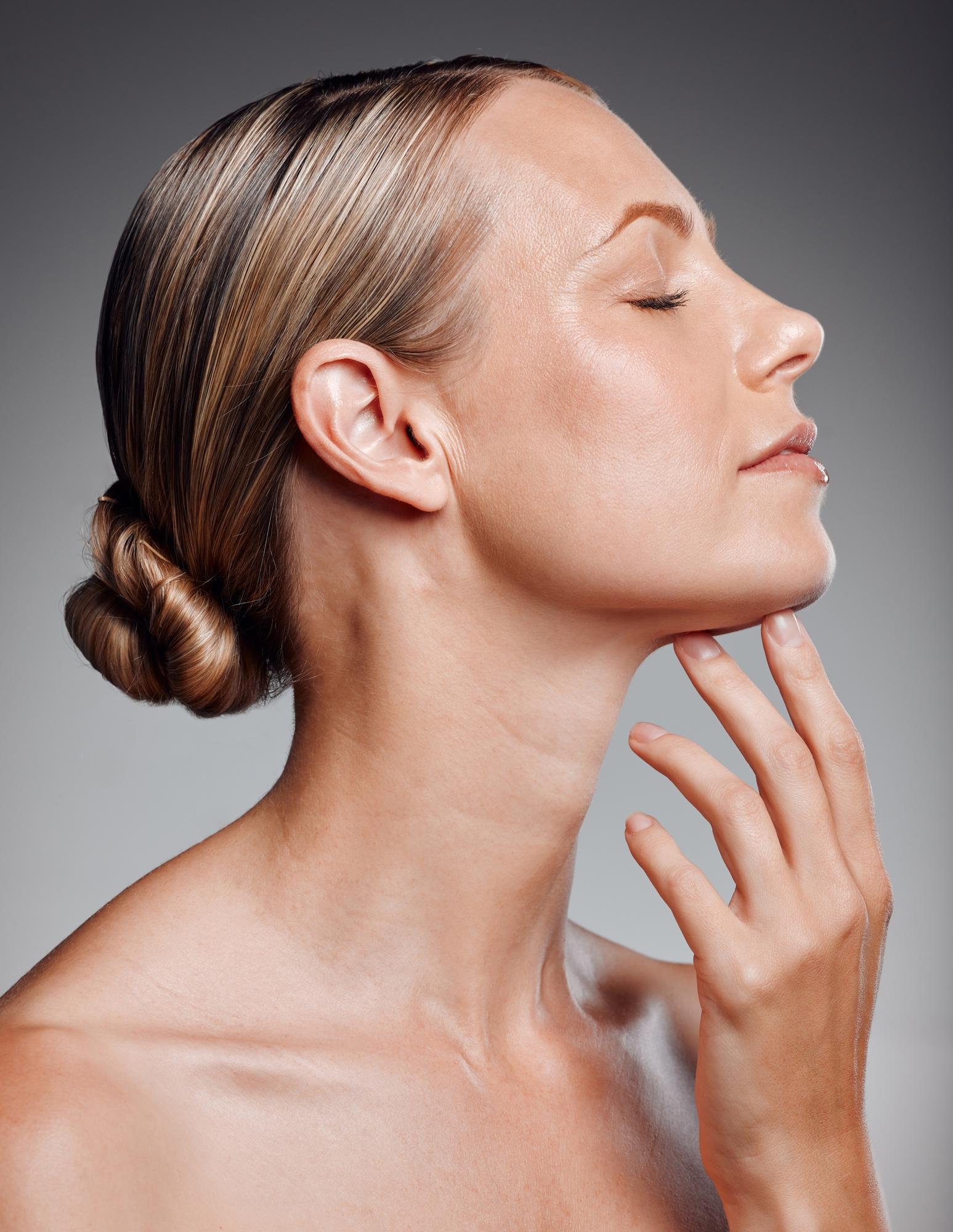 Side-profile studio portrait of a mature woman touching her neck and chin.
