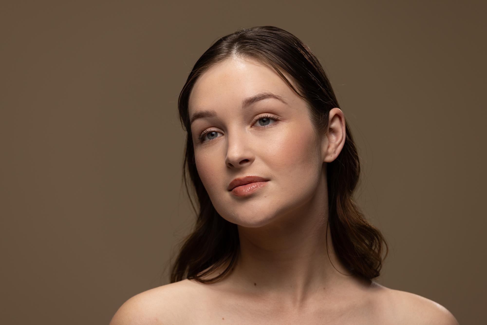 Portrait of a woman with brown hair, soft natural makeup, and a neutral brown studio background.
