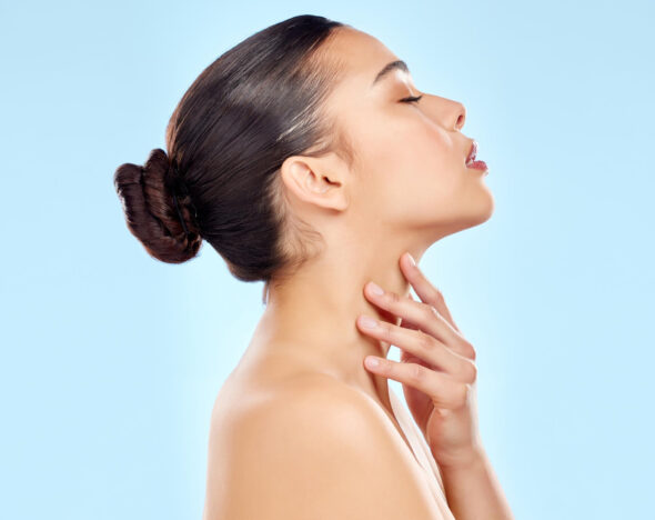 Beauty profile of a woman with smooth skin touching her neck against a light blue background.