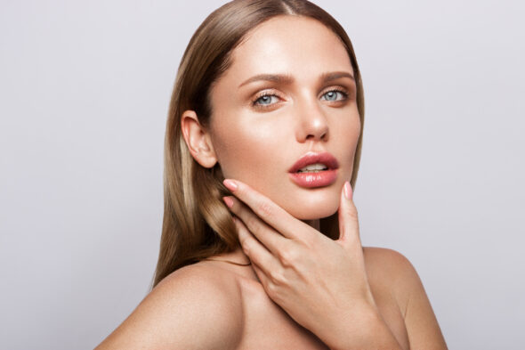 Studio beauty portrait of a woman with glossy pink lips and manicured nails.