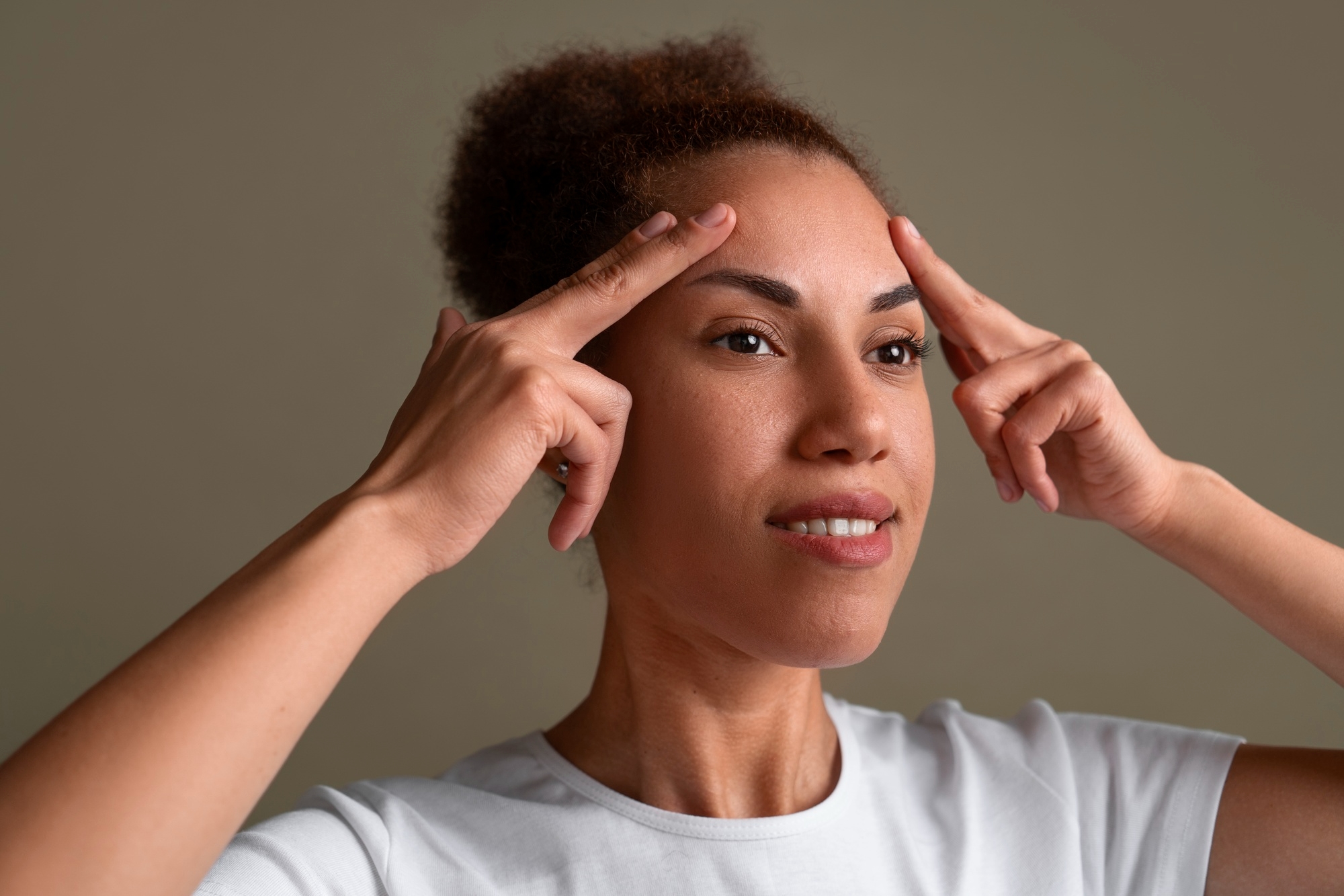 Woman pressing fingers to her forehead and temples while performing a facial massage.