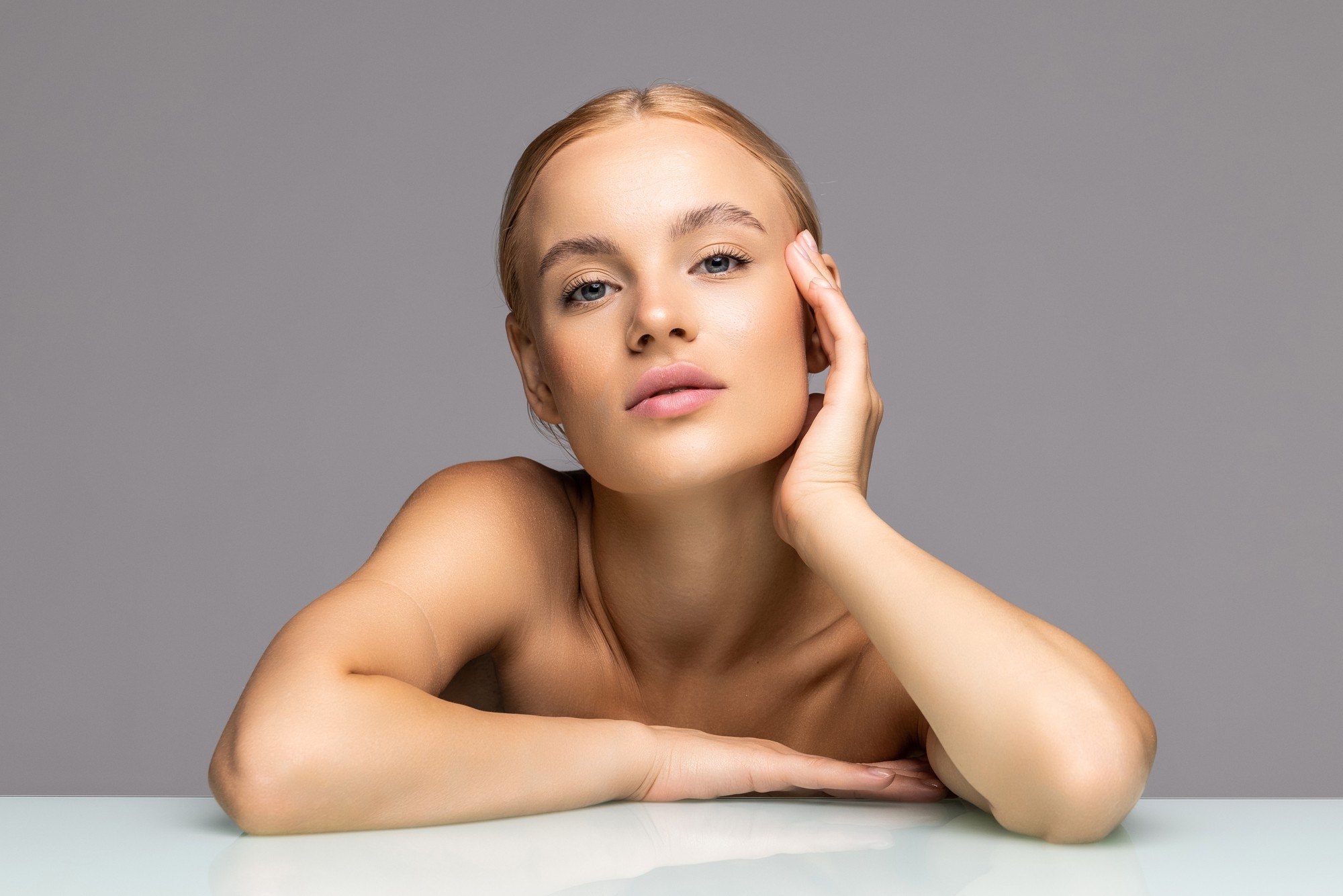 Beauty portrait of a woman resting her hand on her cheek against a gray background.