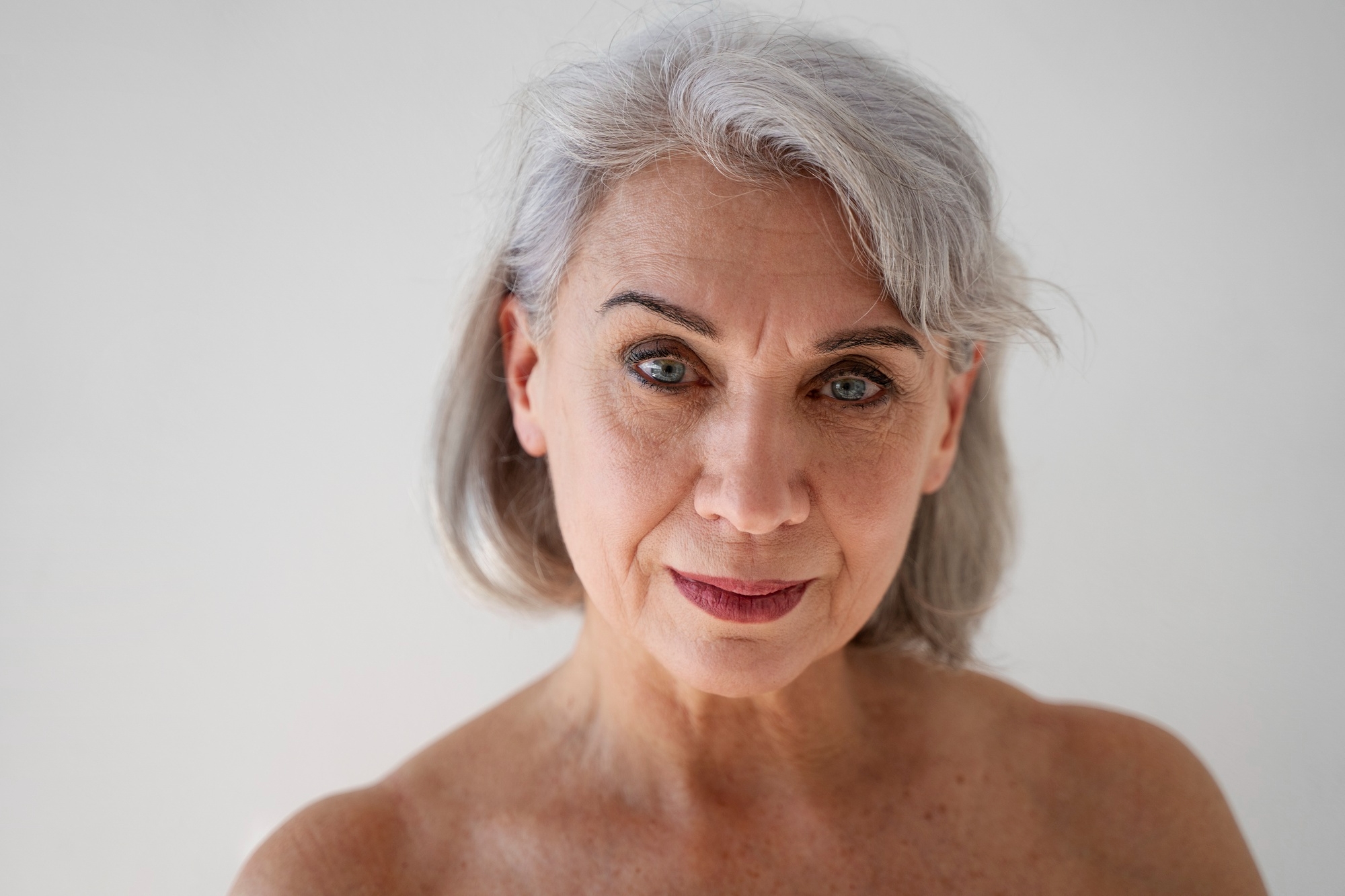 Beauty portrait of an older woman with silver hair and blue eyes against a white background