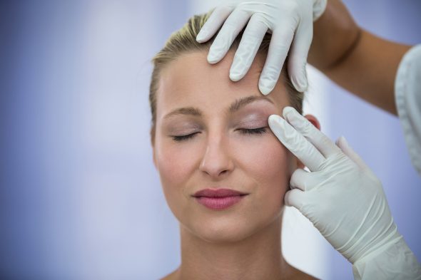 Surgeon in white gloves examining a female patient's eyelid and forehead before blepharoplasty