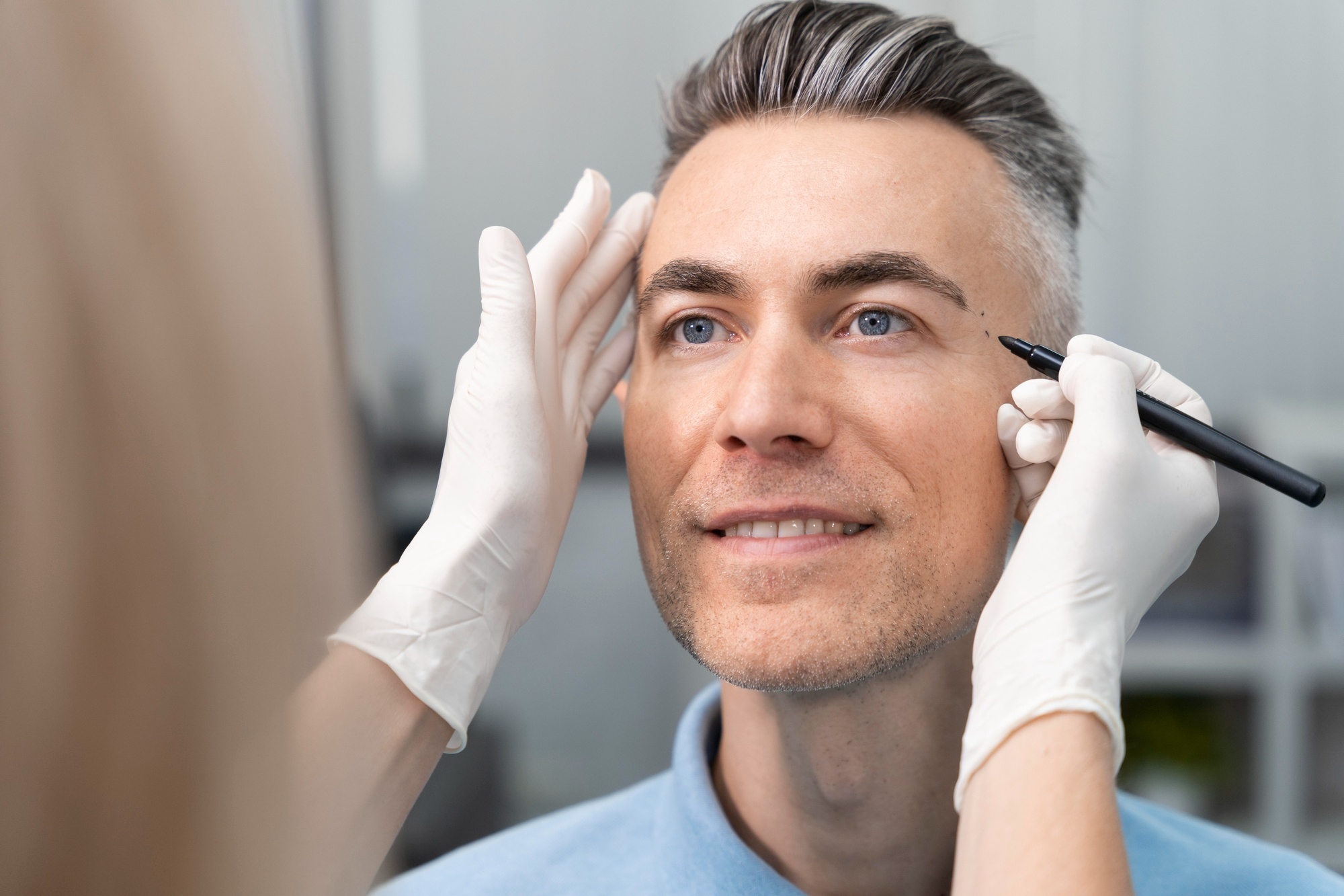 Surgeon in white gloves marking a male patient's eyelid with a pen before blepharoplasty surgery