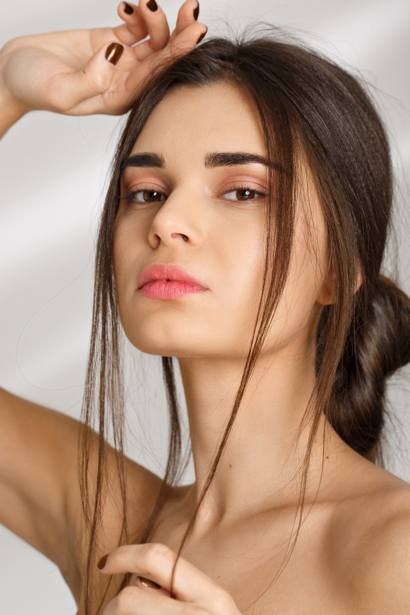 Beauty portrait of a young woman with dark hair posing with her hand above her head against a white background