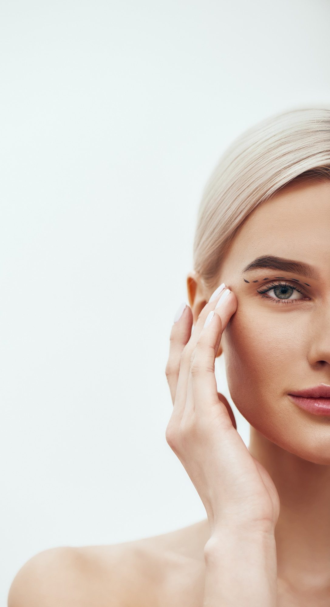 Half-face portrait of a blonde woman touching the corner of her eye against a white background