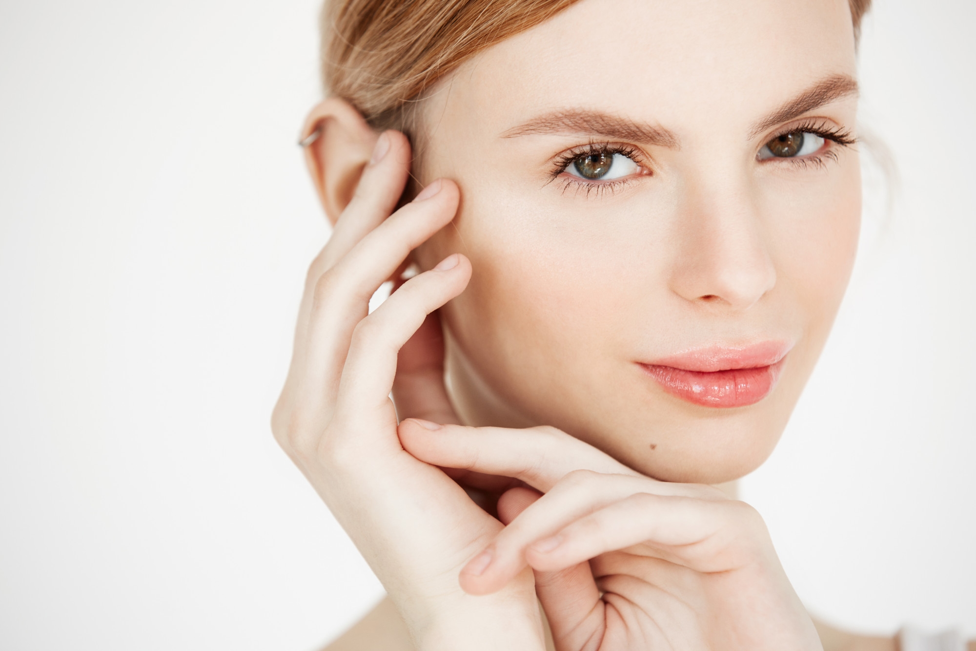 Beauty portrait of a young woman with both hands framing her face against a white background