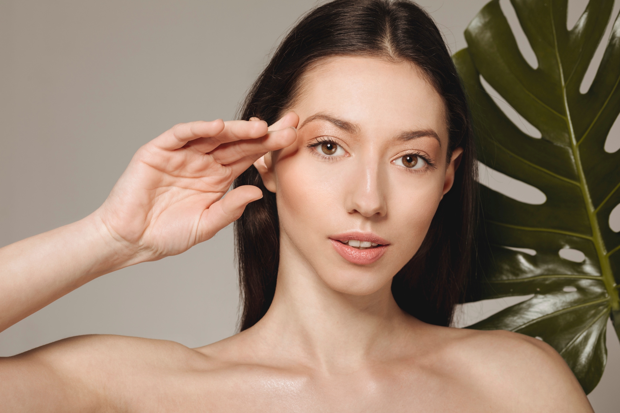 Beauty portrait of a woman touching her eyebrow with a monstera leaf in the background